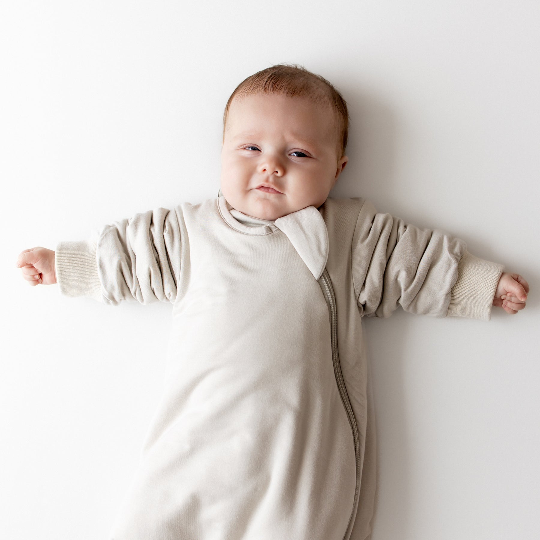 Baby in oat slumber bag on a neutral backdrop