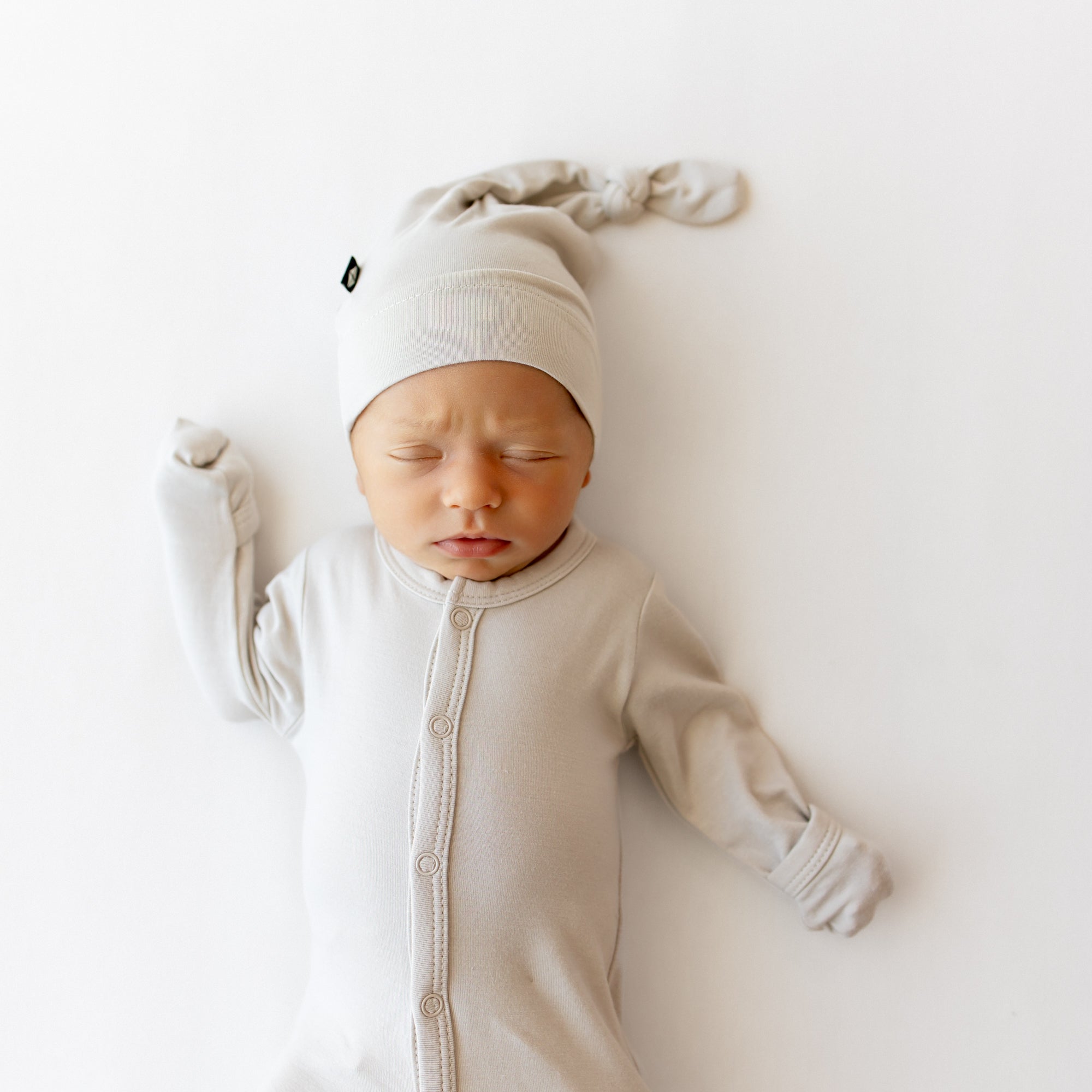 Newborn baby in a beige footie and hat on a white background