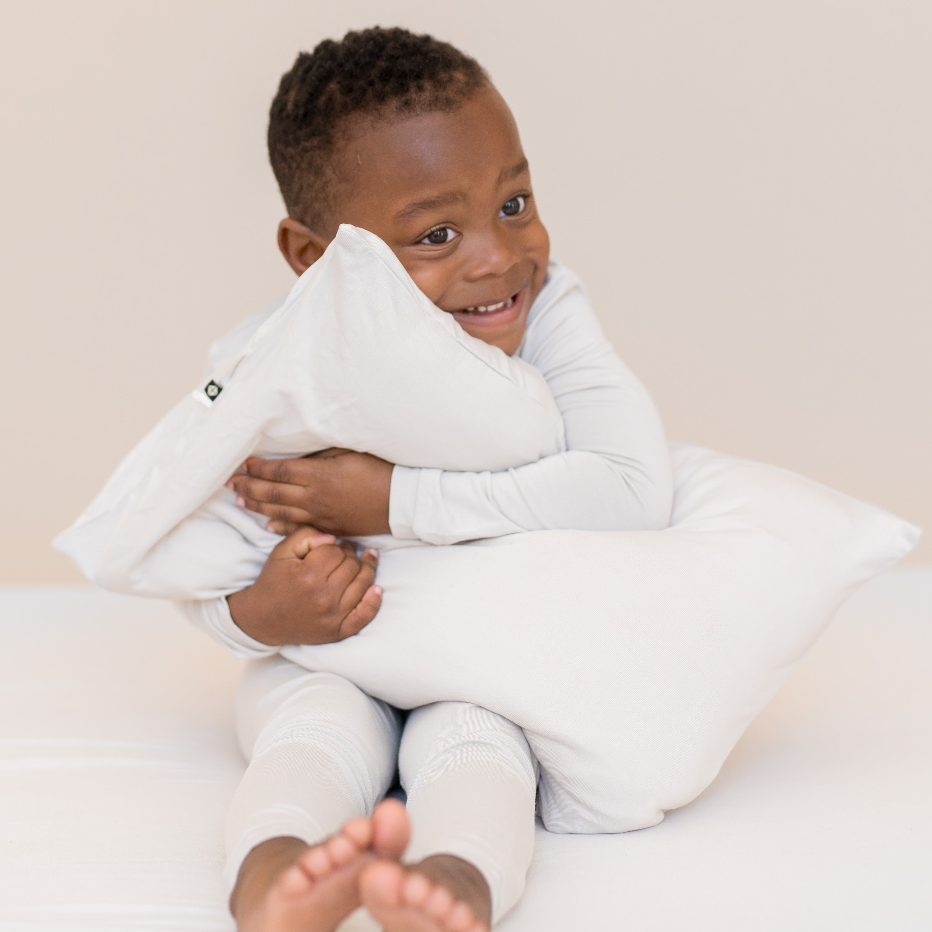 Child hugging an off white pillow on a light-colored background