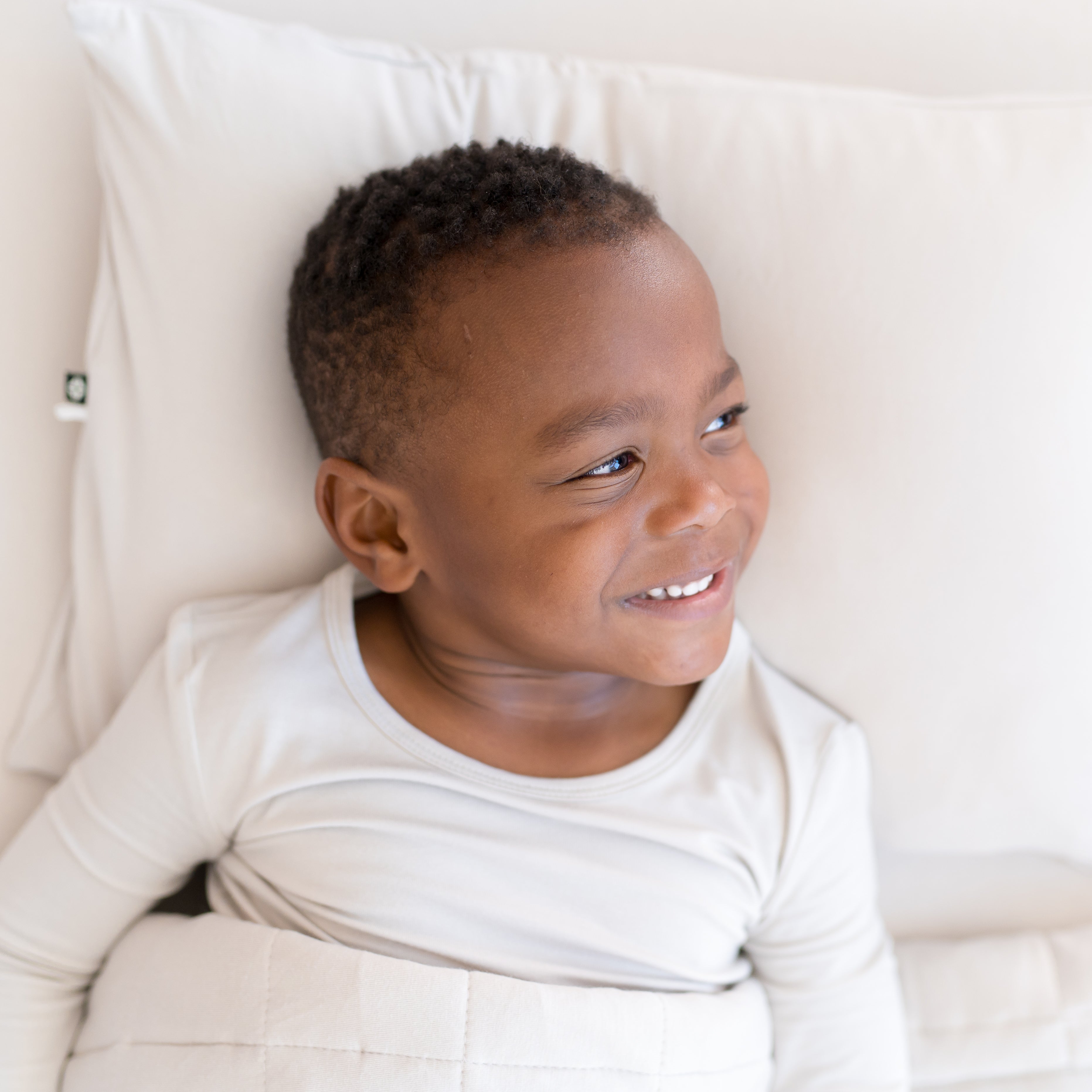 young boy laying in a toddler bed that has an off-white color bedding