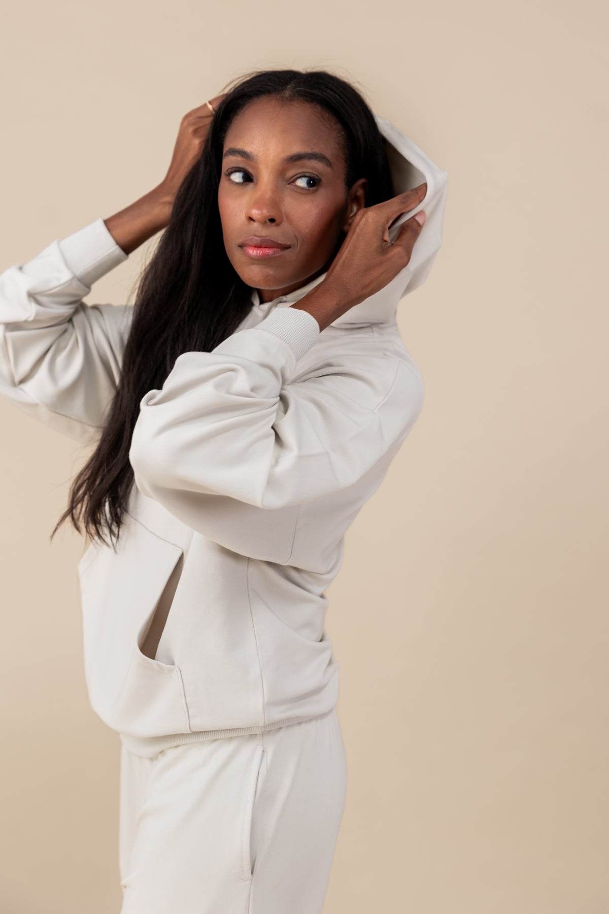 Side pose of Modal wearing Women's Hoodie in Oat color over similar color jogger pants on a beige background