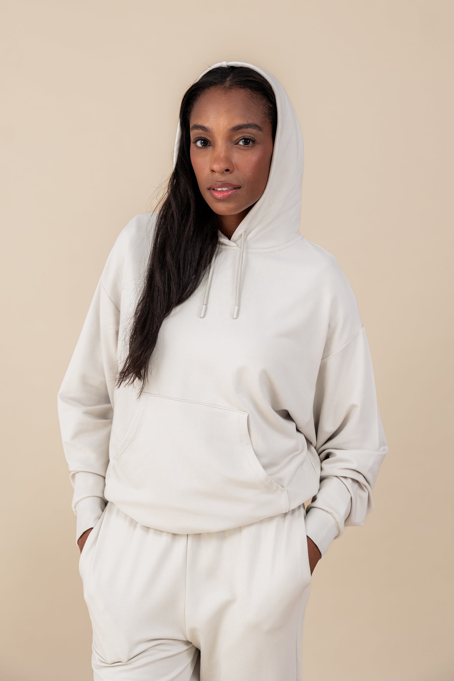 Modal wearing Women's Hoodie in Oat color over similar color jogger pants on a beige background