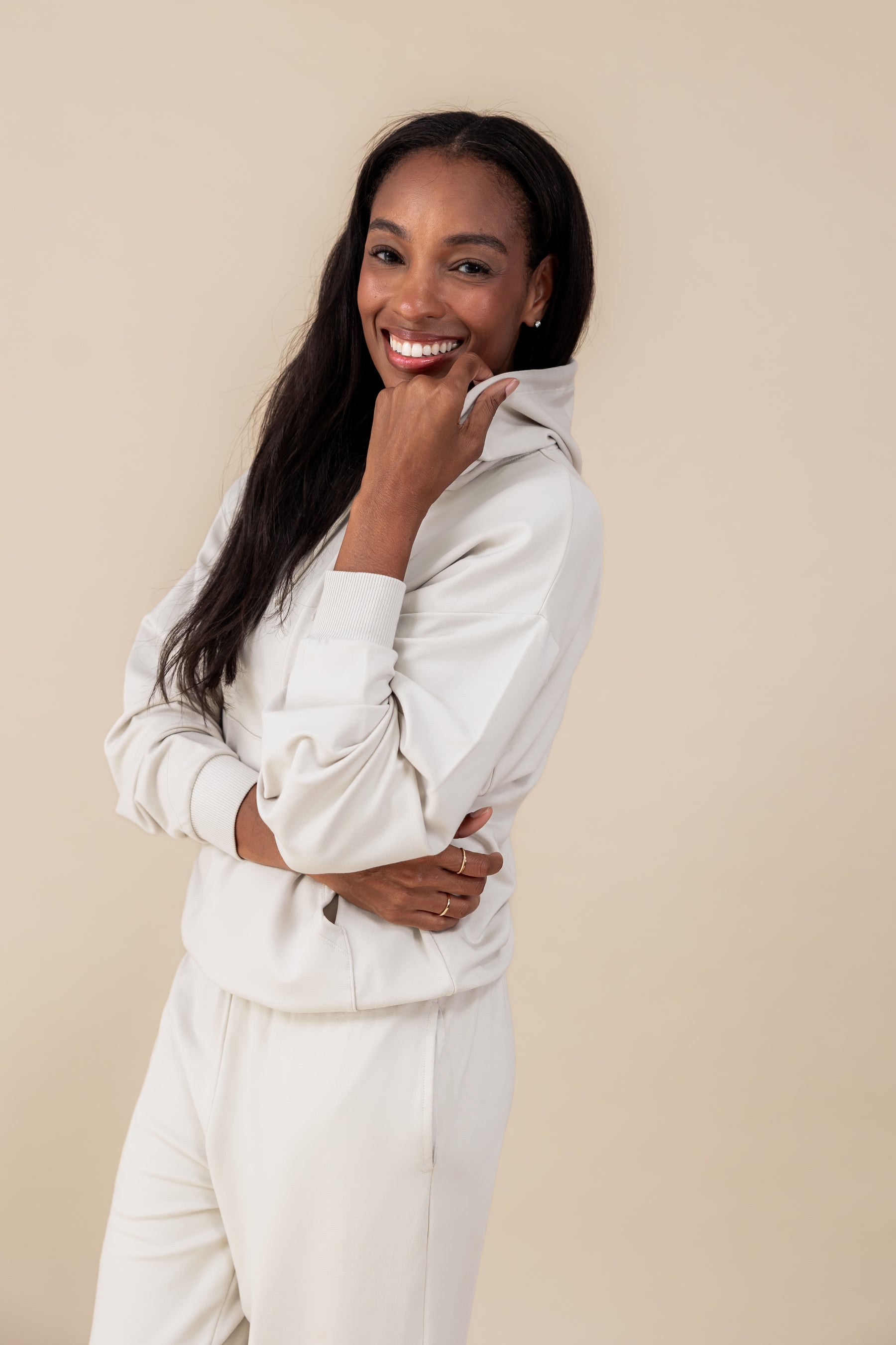 Modal smiling wearing Women's Hoodie in Oat color over similar color jogger pants on a beige background