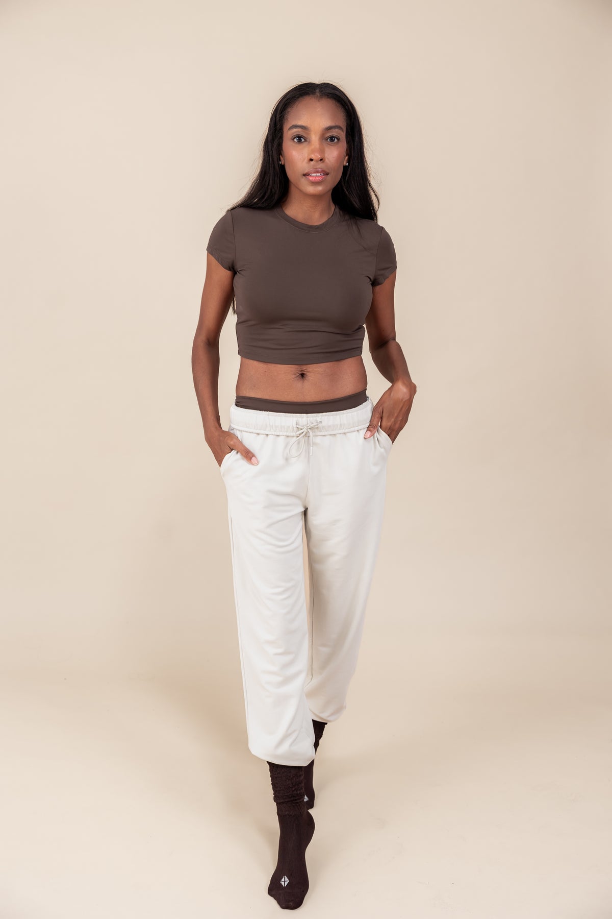 Woman wearing Women's Jogger Pants in Oat color under a brown shirt on a beige background