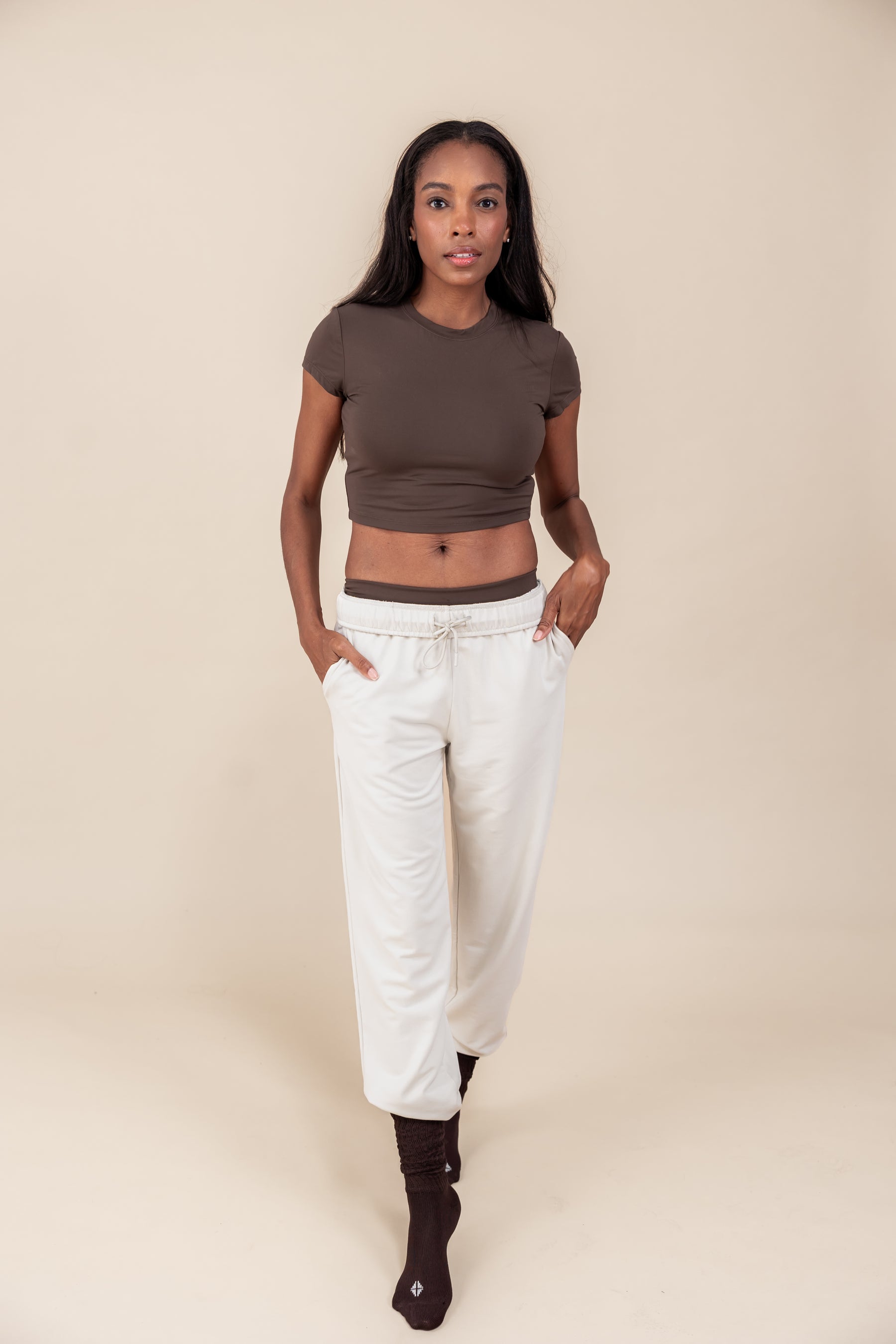Woman wearing Women's Jogger Pants in Oat color under a brown shirt on a beige background