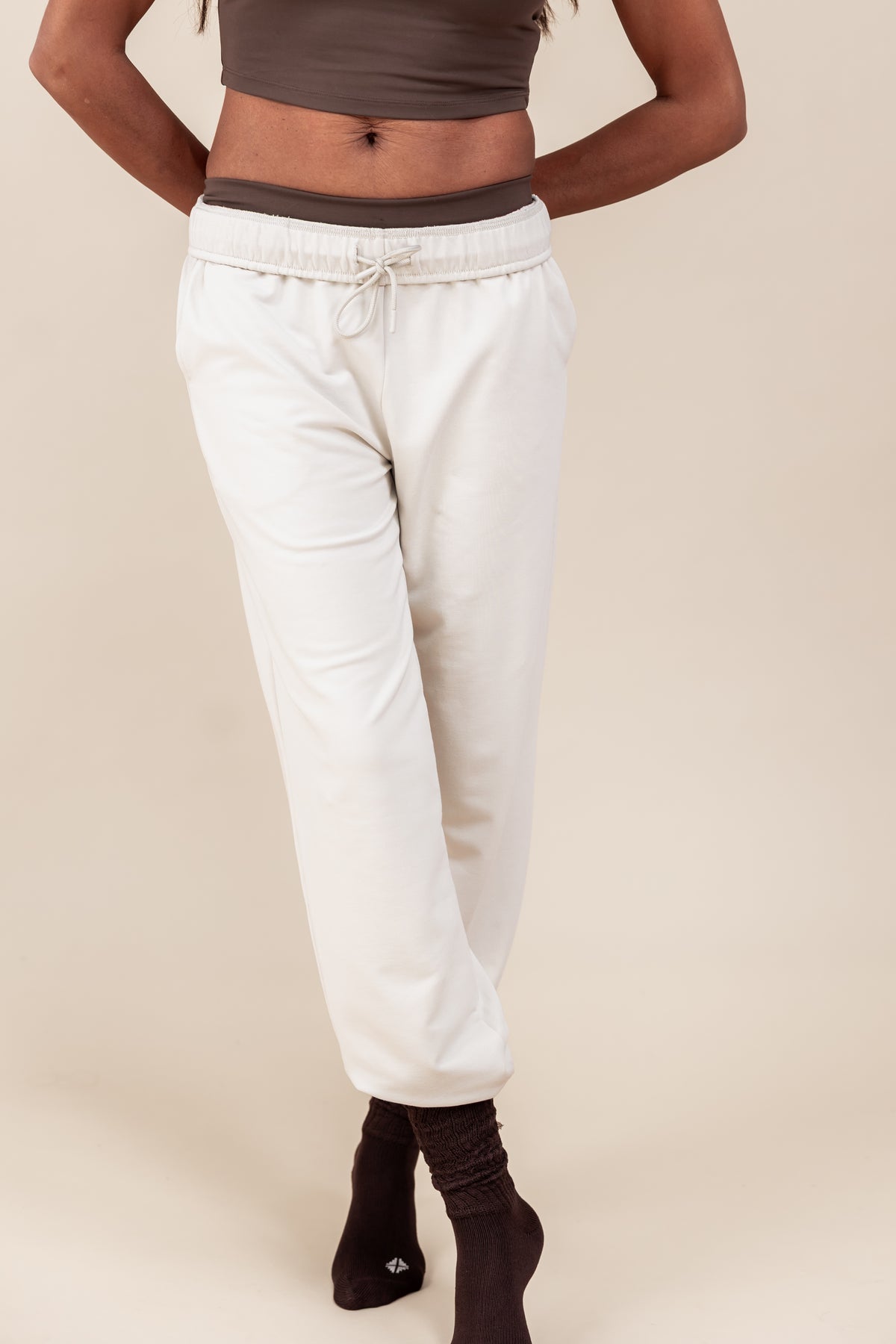 Woman wearing Women's Jogger Pants in Oat color under a brown shirt on a beige background