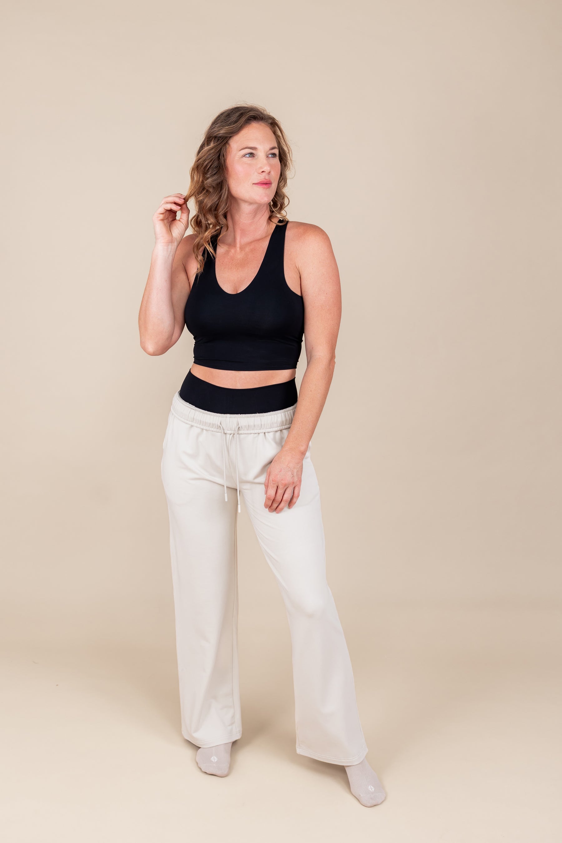 Woman posing in Women's Sweatpants in Oat color under black flex bra tank on a beige background
