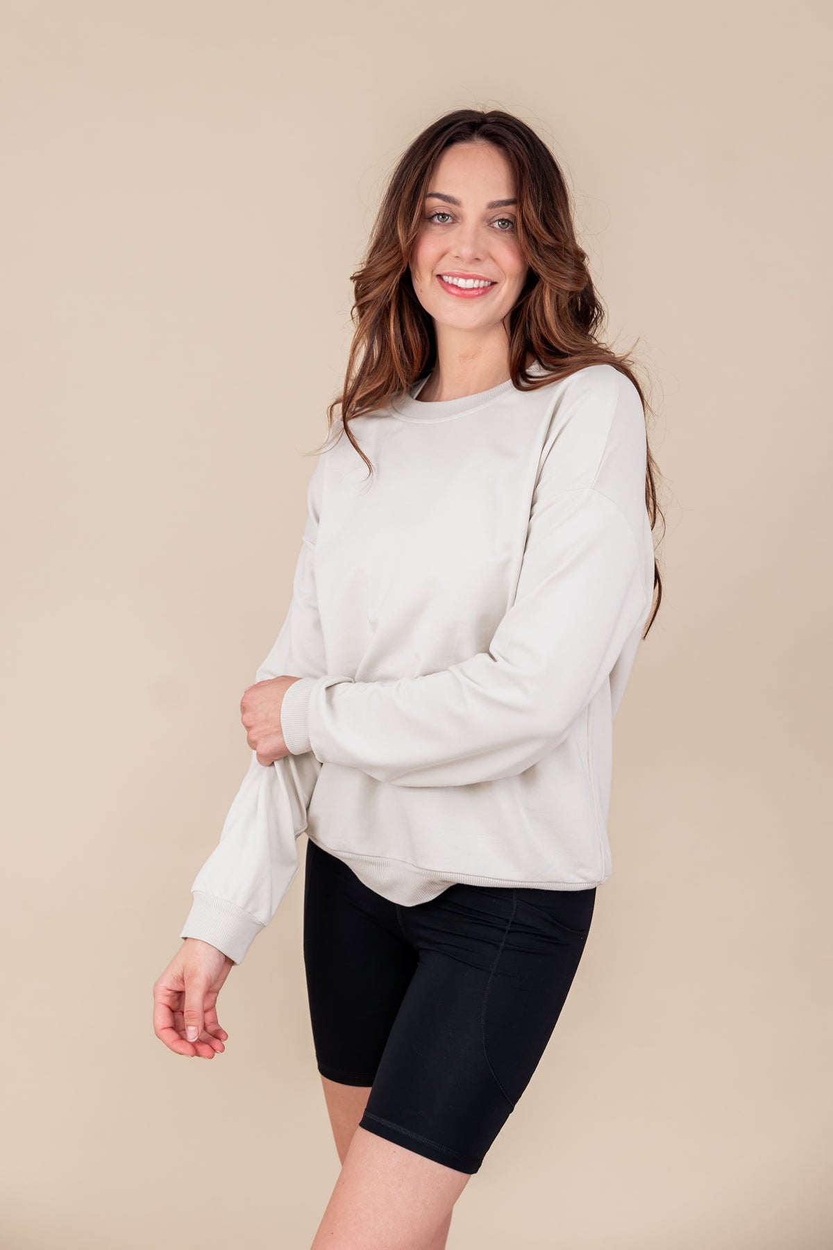 Woman wearing Women's Sweatshirt in Oat color over black shorts on a beige background