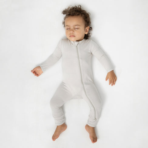 Sleeping toddler laying in a crib on a white crib sheet wearing the Zippered Romper in Oat