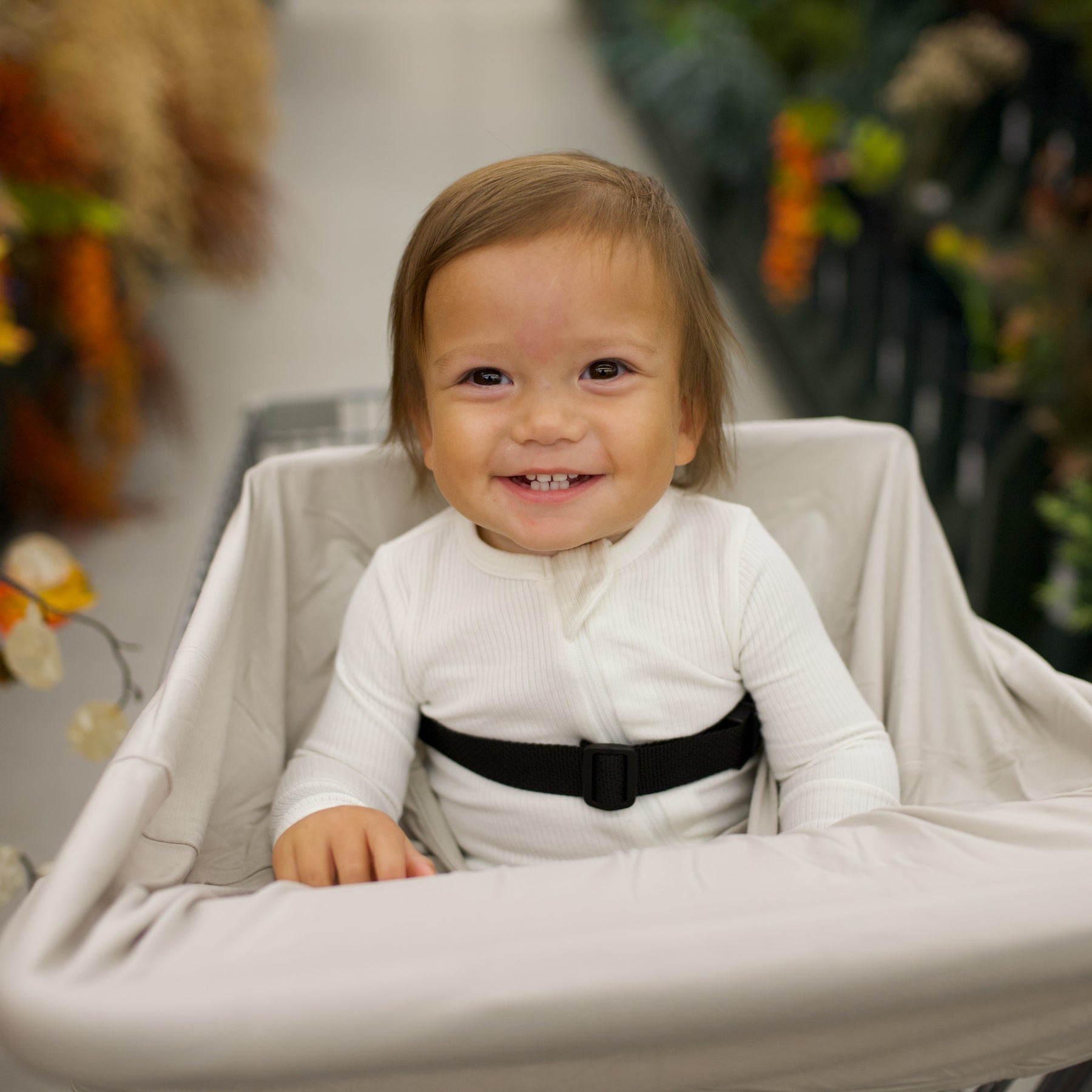 Child in a shopping cart with a cover on the cart with a blurred floral background