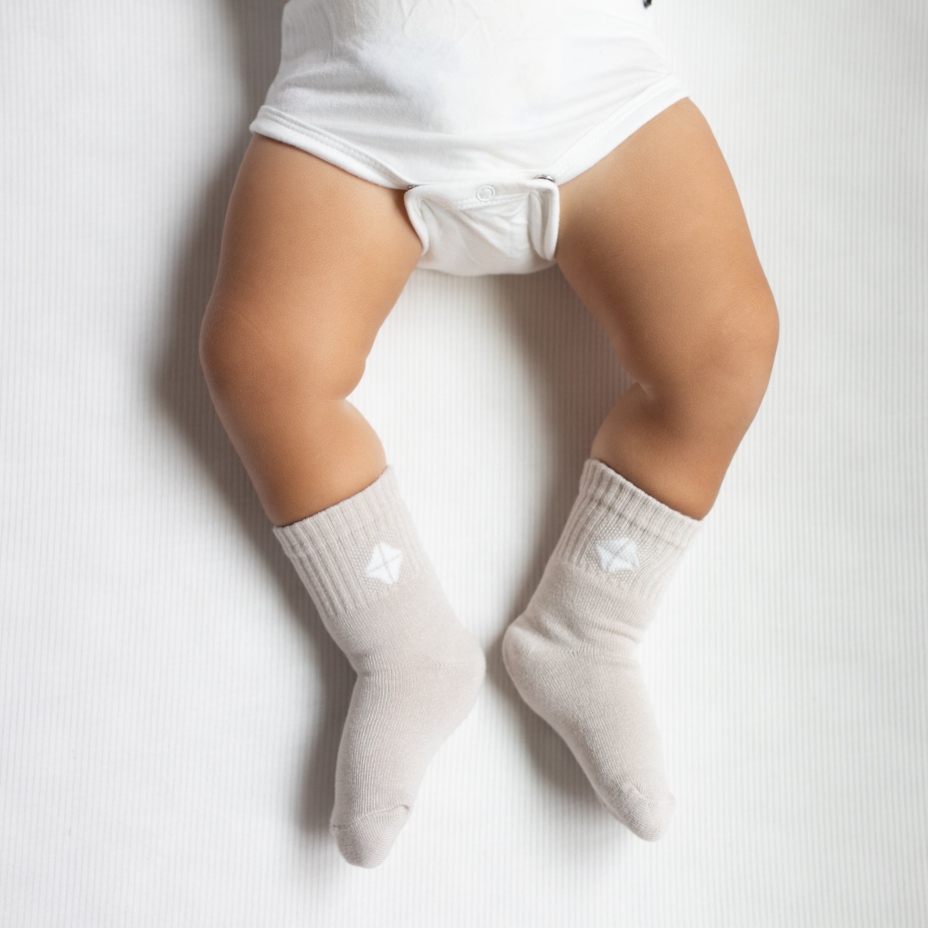 Crew Socks in Oat shown on an infant model with the Kyte Baby logo visible