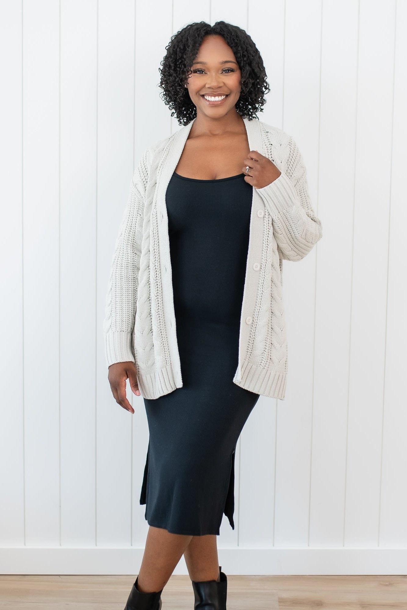 Smiling female model wearing the Cable Knit Adult Cardigan in Oat with a Women's Cami Dress in Midnight on underneath