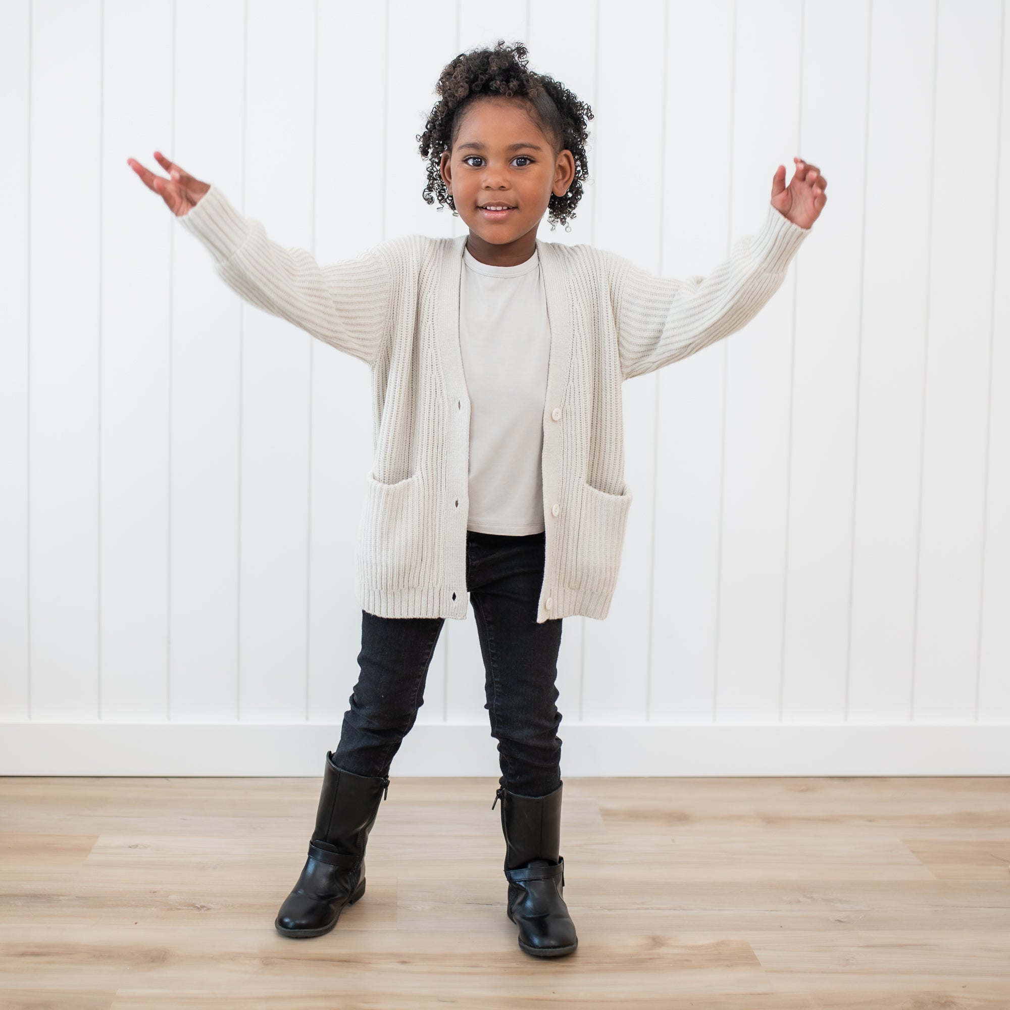 Young girl wearing the Chunky Knit Oversized Cardigan in Oat with black pants and black boots