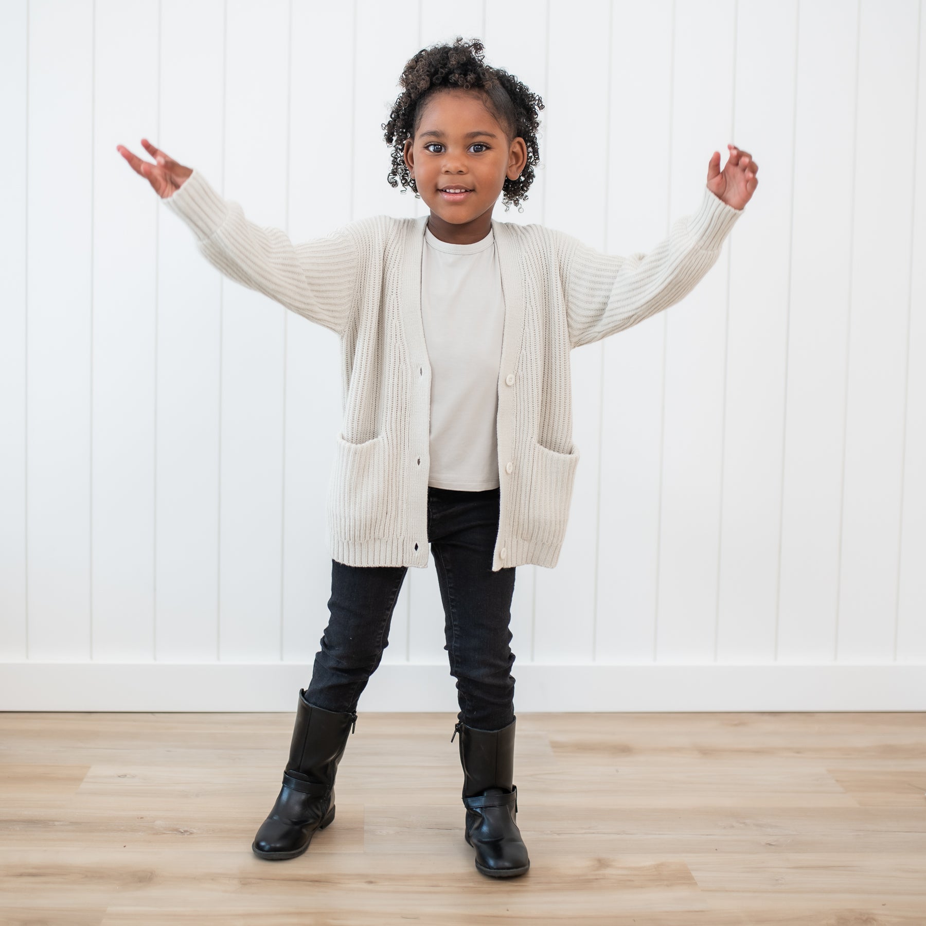 Young girl wearing the Chunky Knit Oversized Cardigan in Oat with black pants and black boots