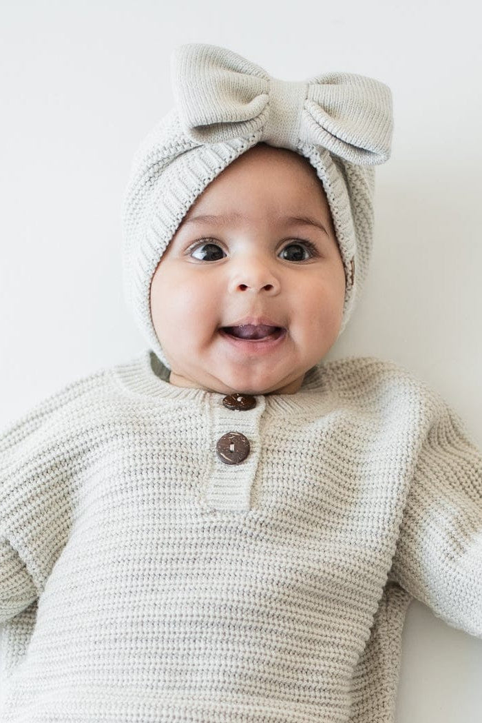 Infant laying down wearing the Chunky Knit Bow Headband in Oat and matching chunky knit romper and knit booties