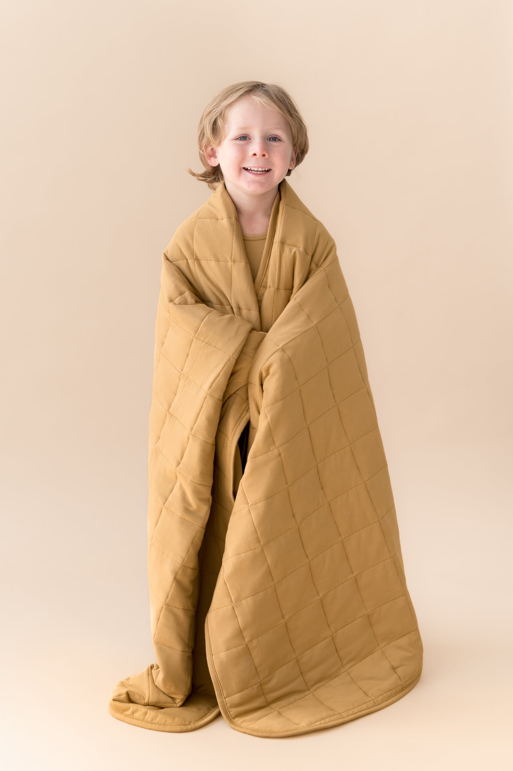 Child wrapped in Toddler Blanket in Ochre 2.5 on a beige background