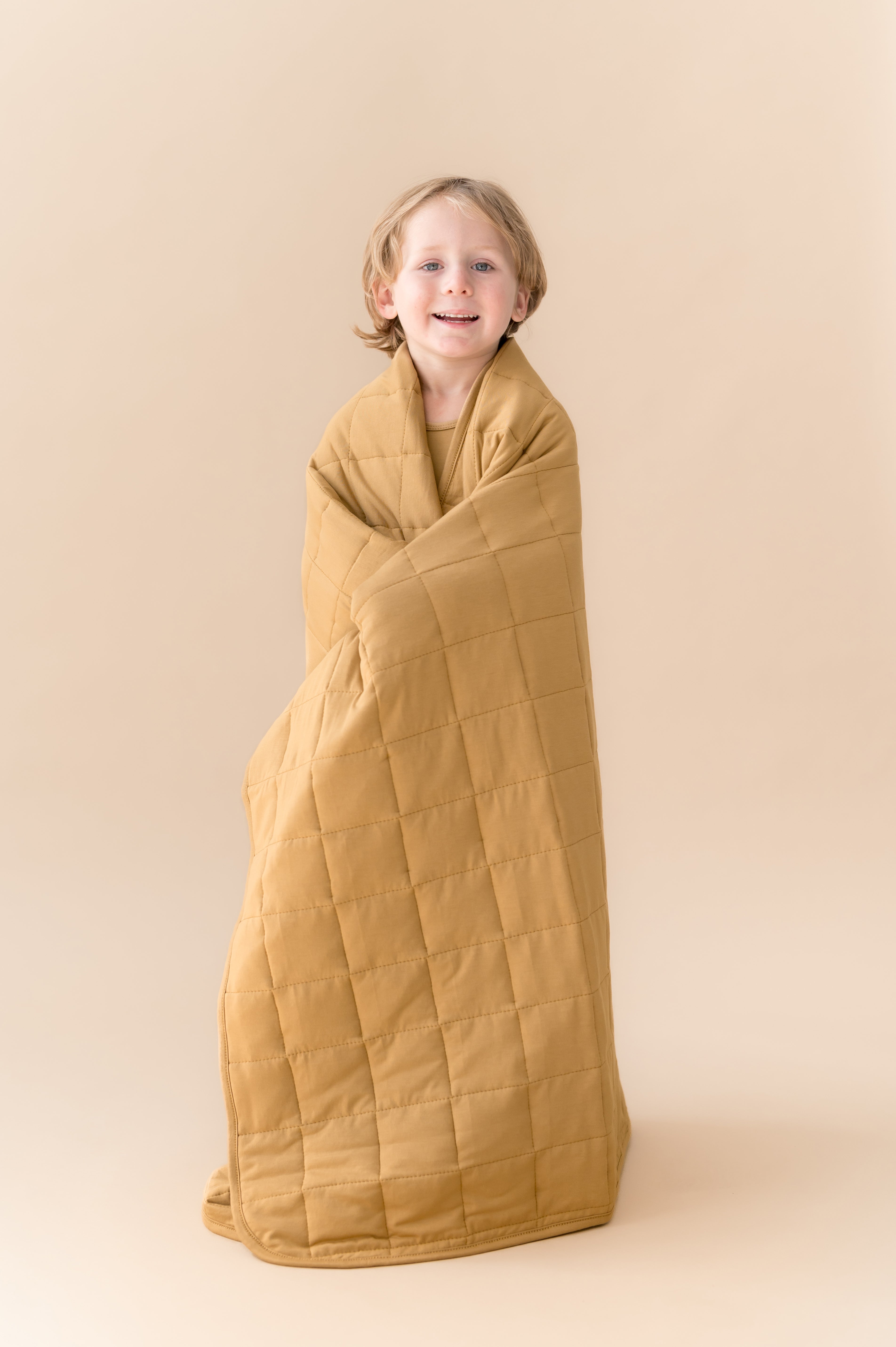 Child wrapped in Toddler Blanket in Ochre 2.5 on a beige background
