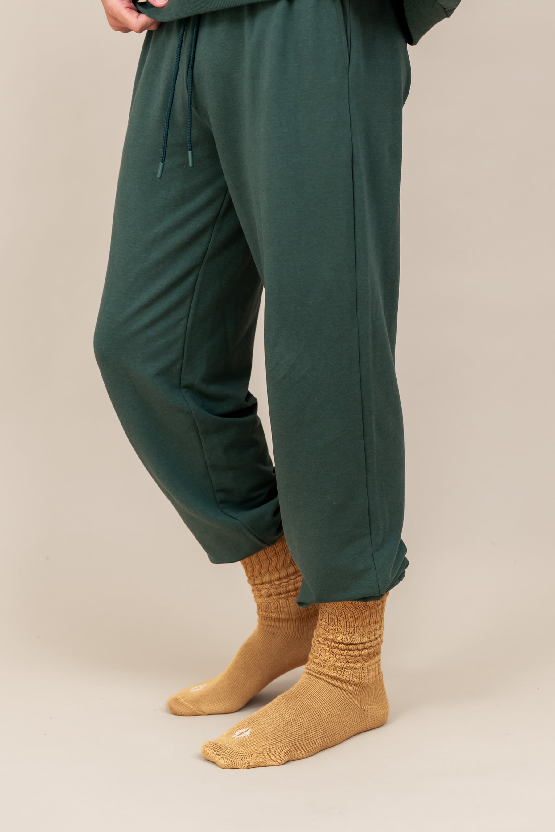 Modal wearing Adult Scrunch Socks in Ochre color while wearing green jogger set on a beige background