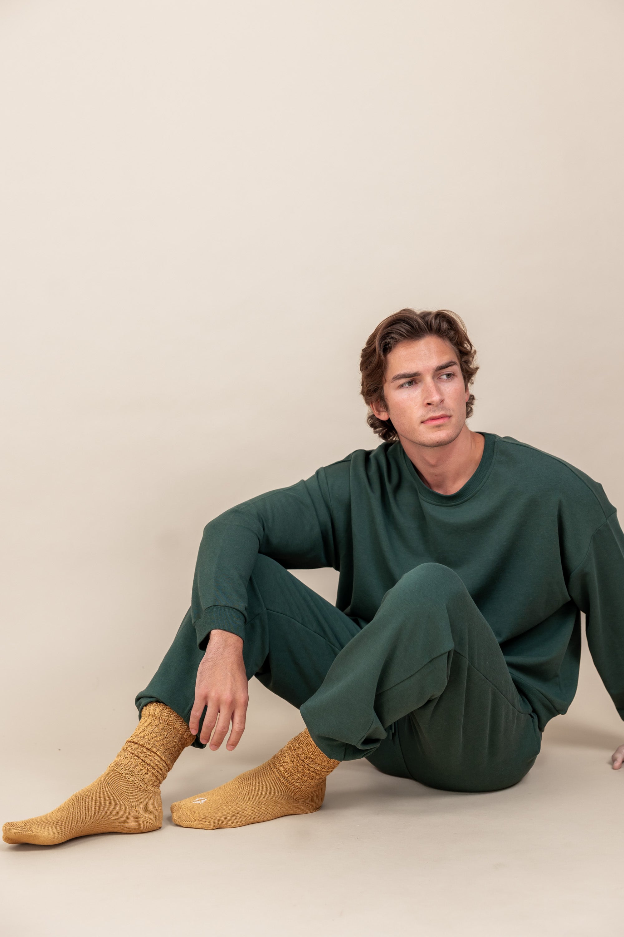 Modal sitting on beige floor while wearing Adult Scrunch Socks in Ochre color and green jogger set