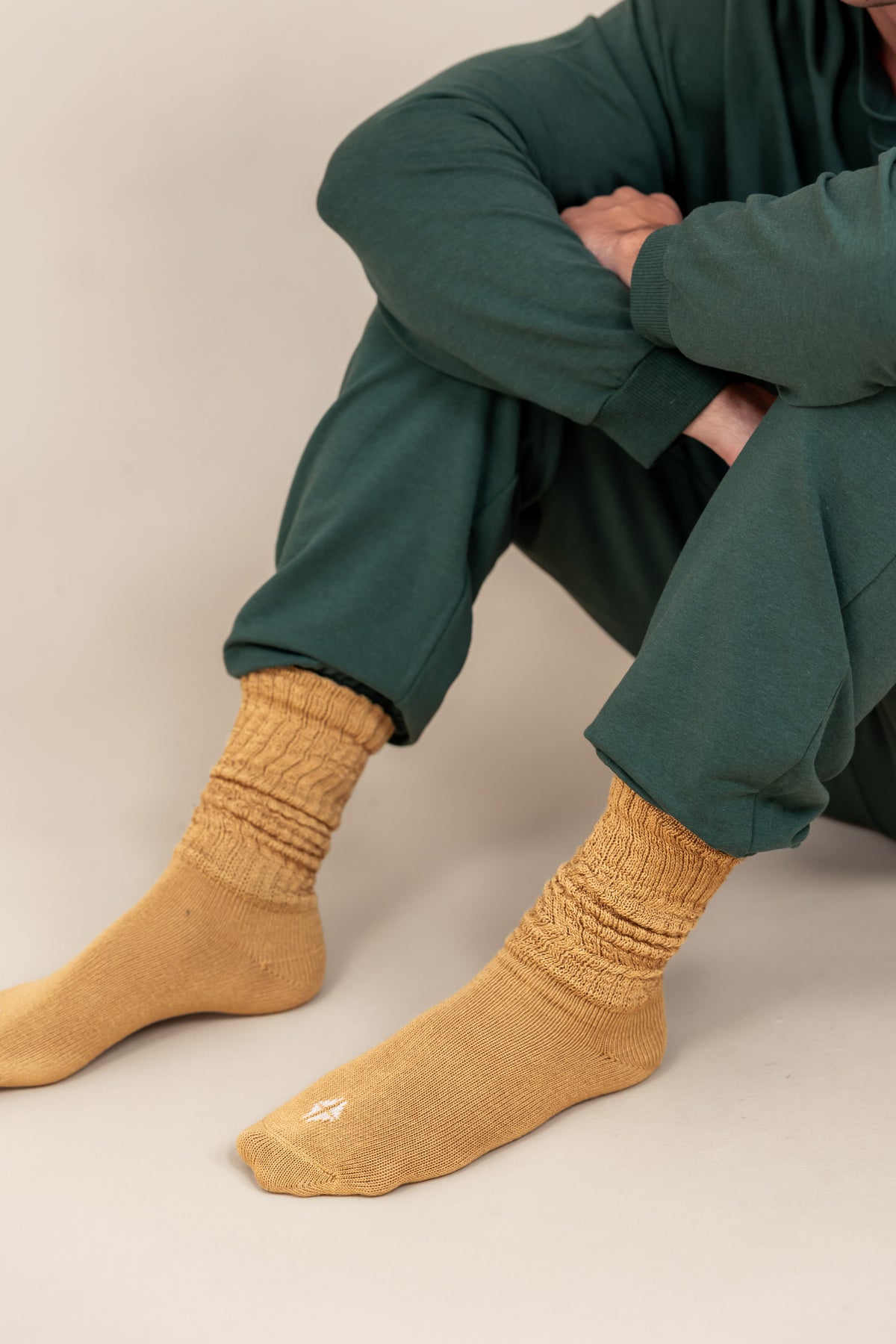 Modal wearing Adult Scrunch Socks in Ochre color while wearing green jogger set on a beige background