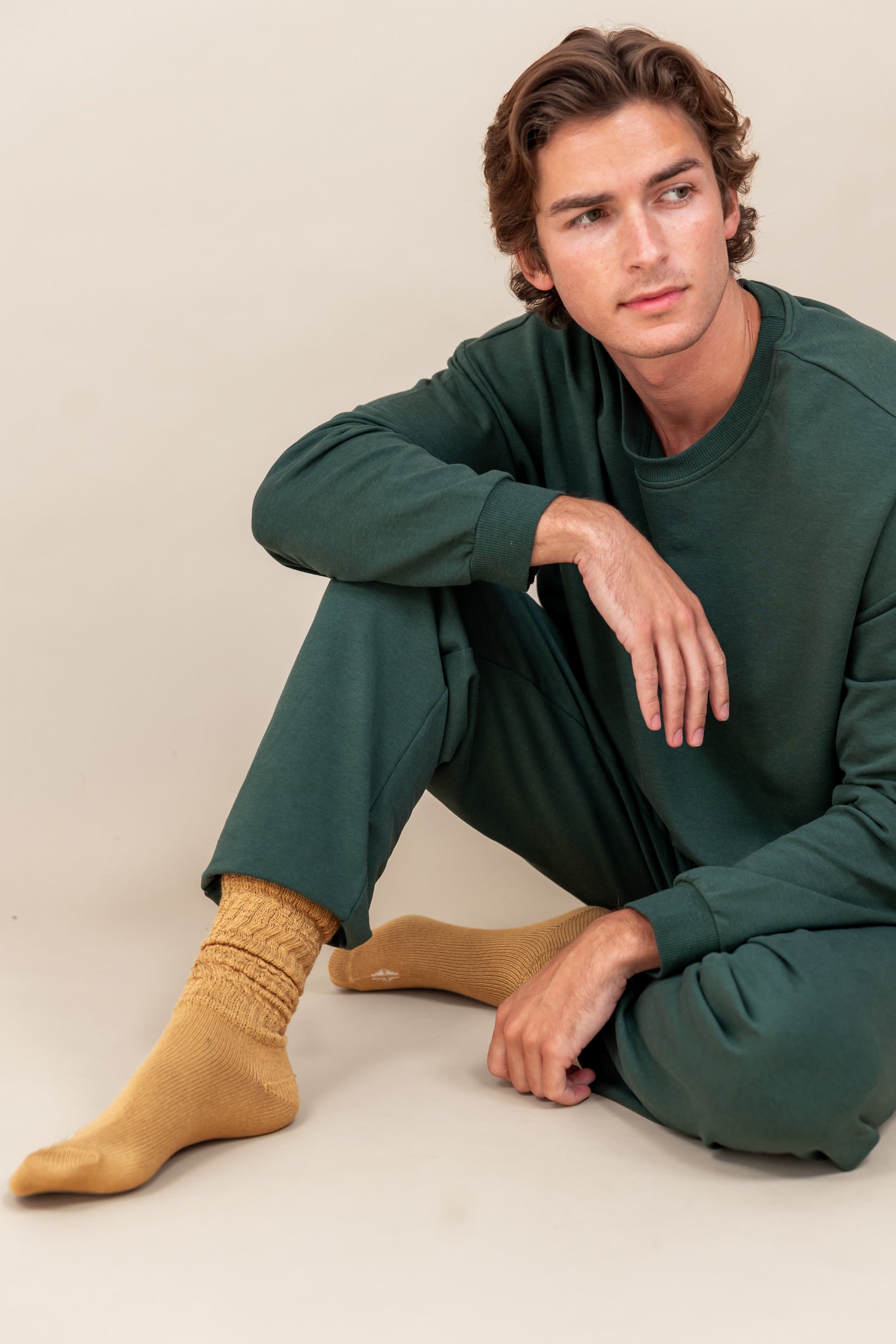 Modal wearing Adult Scrunch Socks in Ochre color while wearing green jogger set while sitting on a beige background
