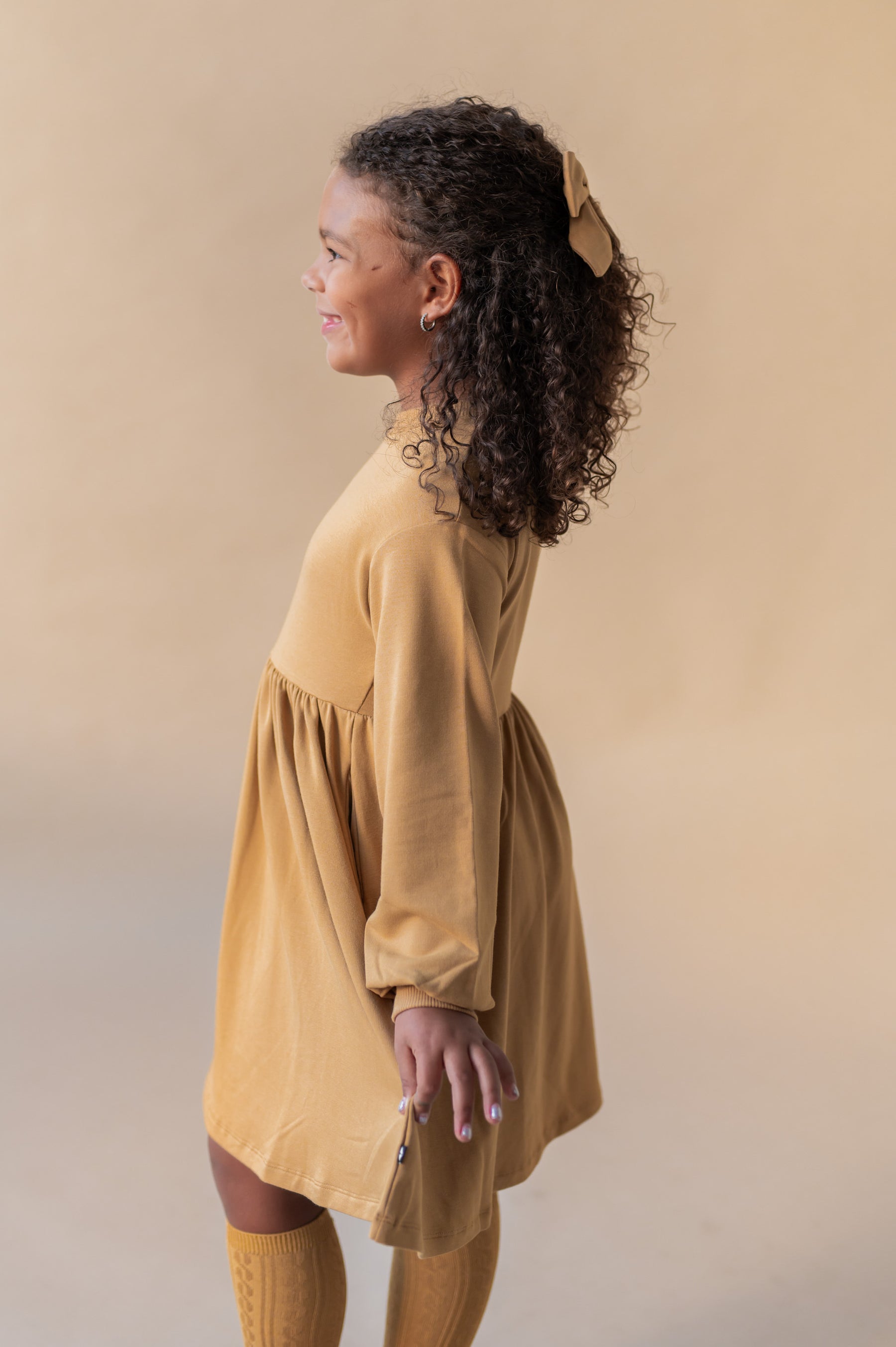 Side pose of Girl wearing Long Sleeve Skater Dress in Ochre color on a beige background