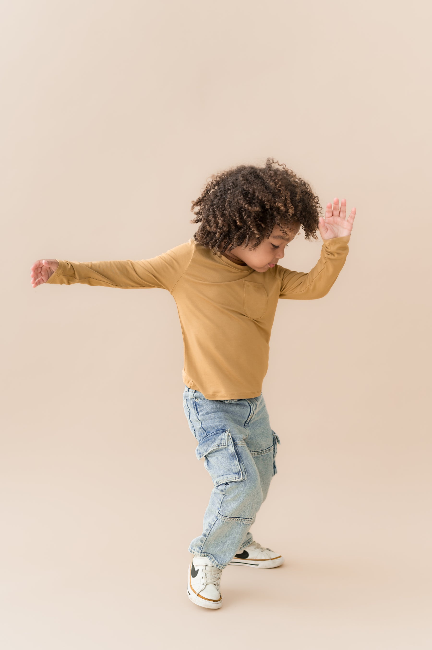 Boy moving in Long Sleeve Toddler Crew Neck Tee in Ochre over blue jeans on a beige background