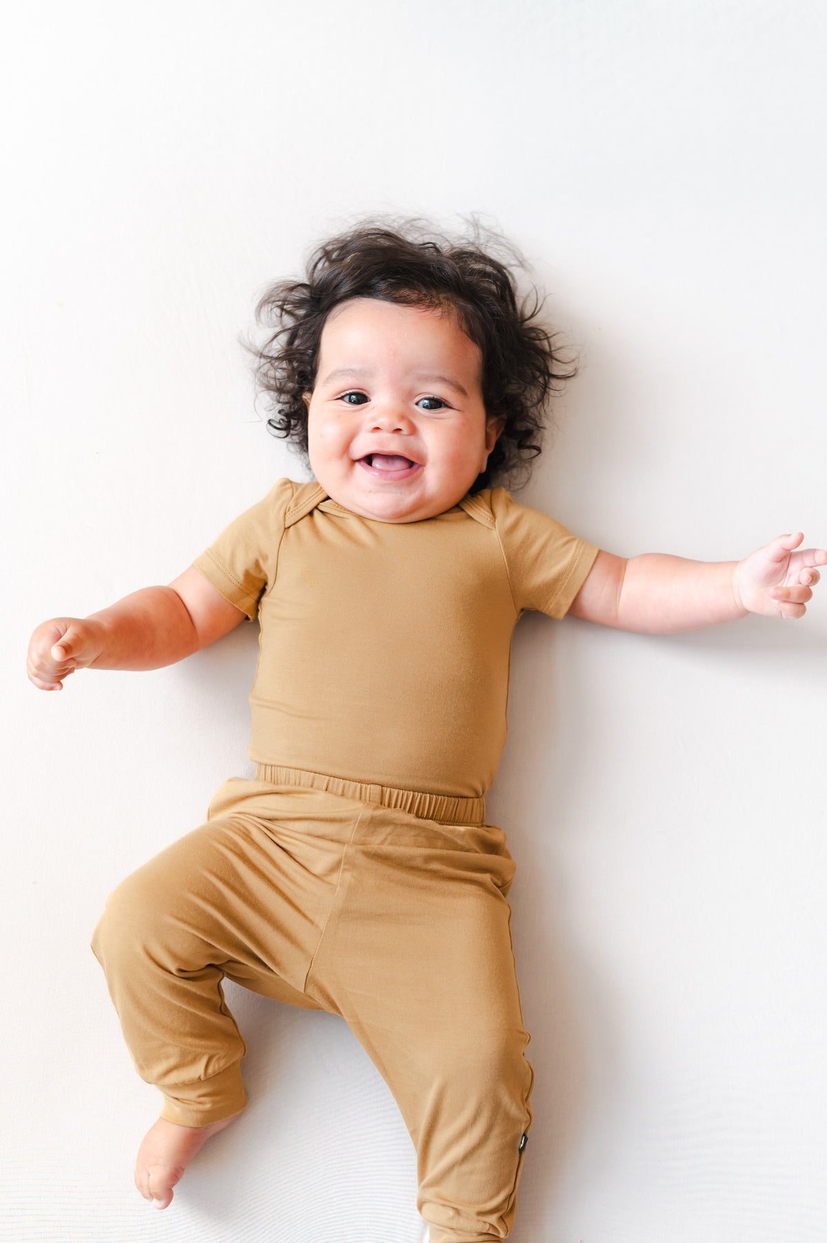 Baby wearing Pant in Ochre over similar color bodysuit on a beige background
