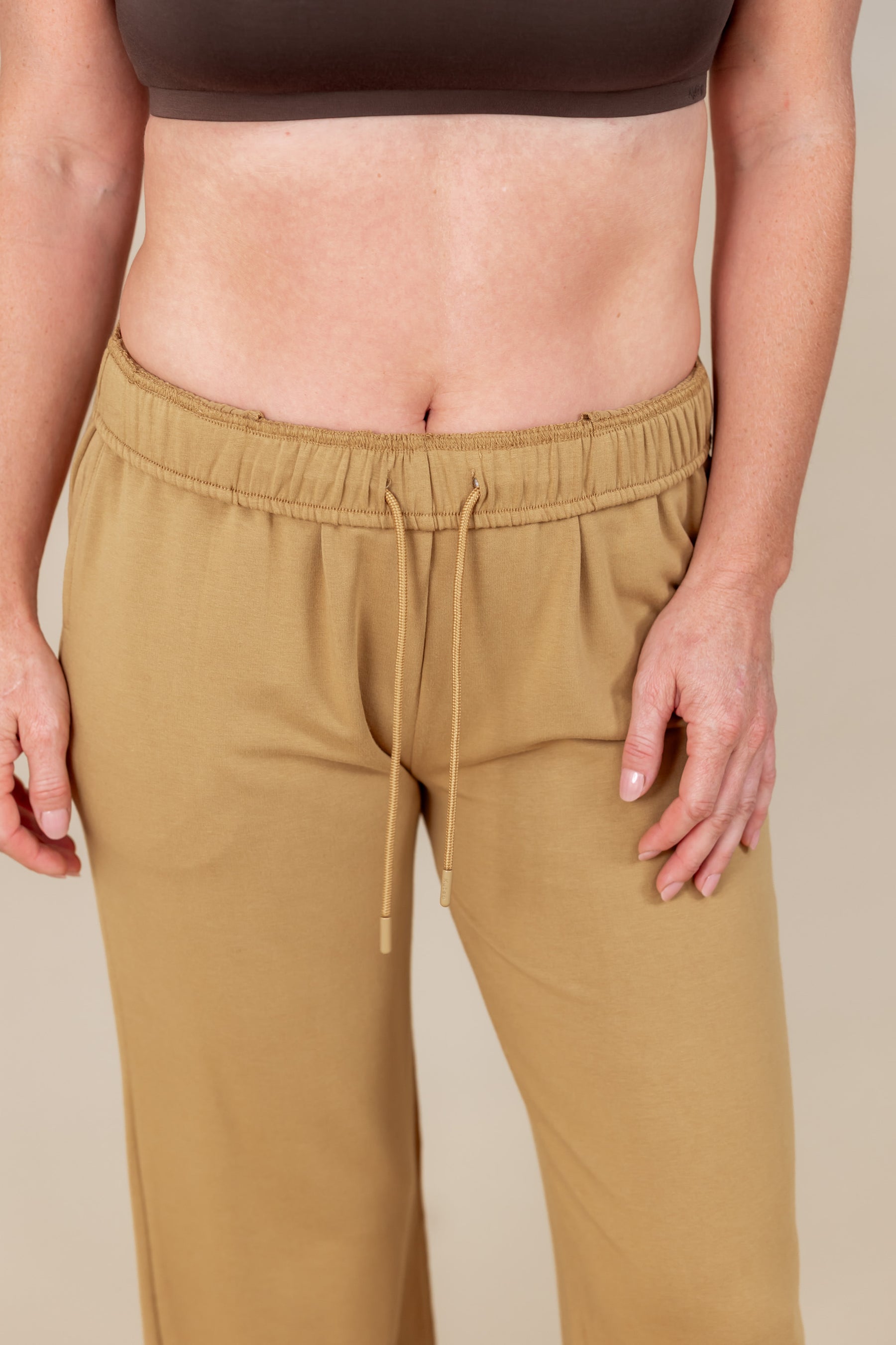 Modal wearing Women's Sweatpants in Ochre color under brown tank top on a white background