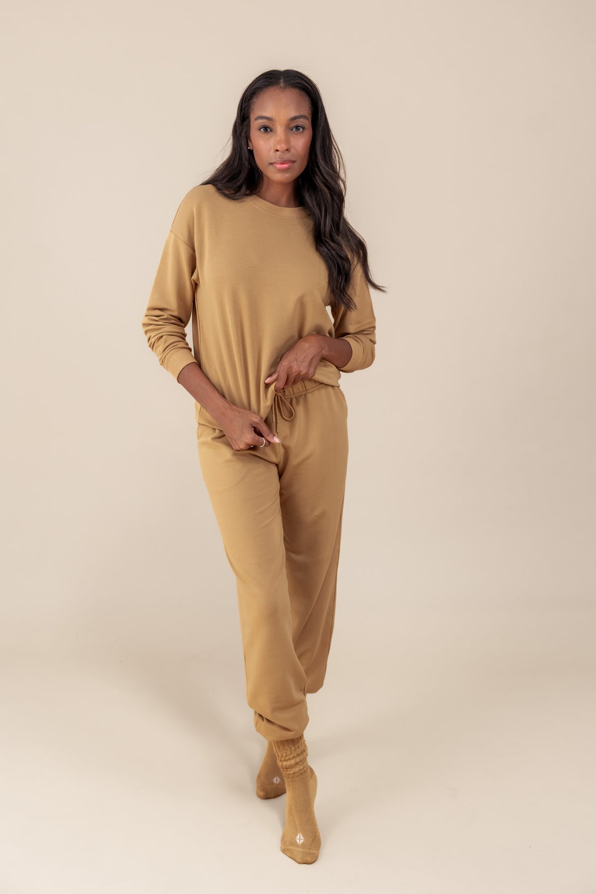 Modal wearing Women's Jogger Pants in Ochre color under similar color women's sweatshirt on a beige background