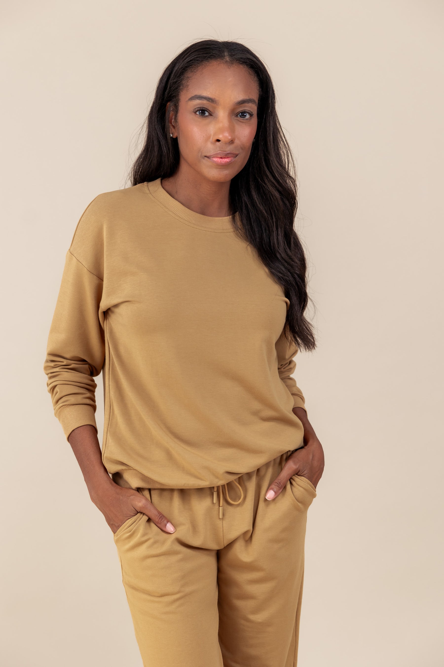 Woman wearing Women's Sweatshirt in Ochre color over similar color jogger pants on a beige background