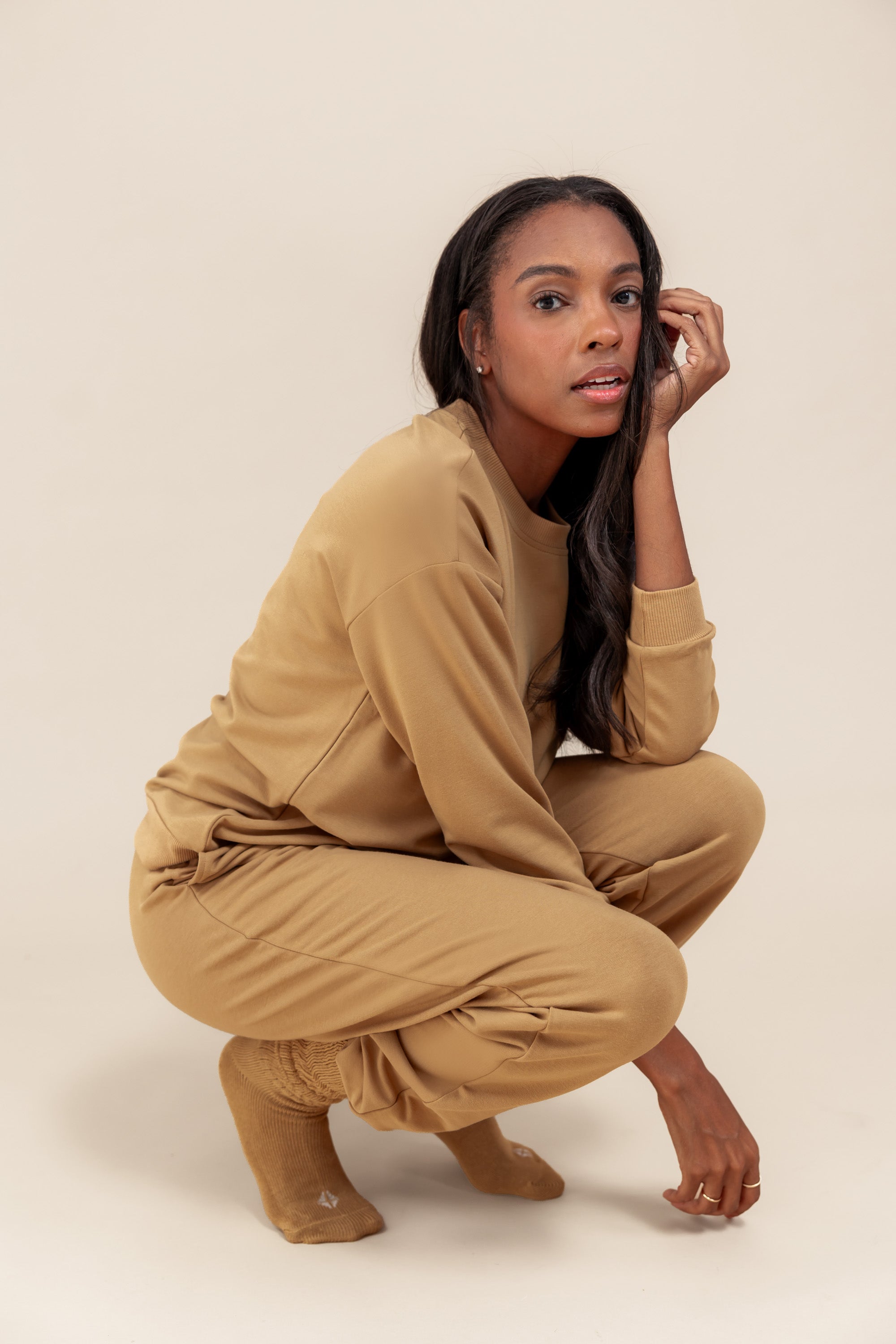 Modal posing in Women's Jogger Pants in Ochre color under similar color women's sweatshirt on a beige background