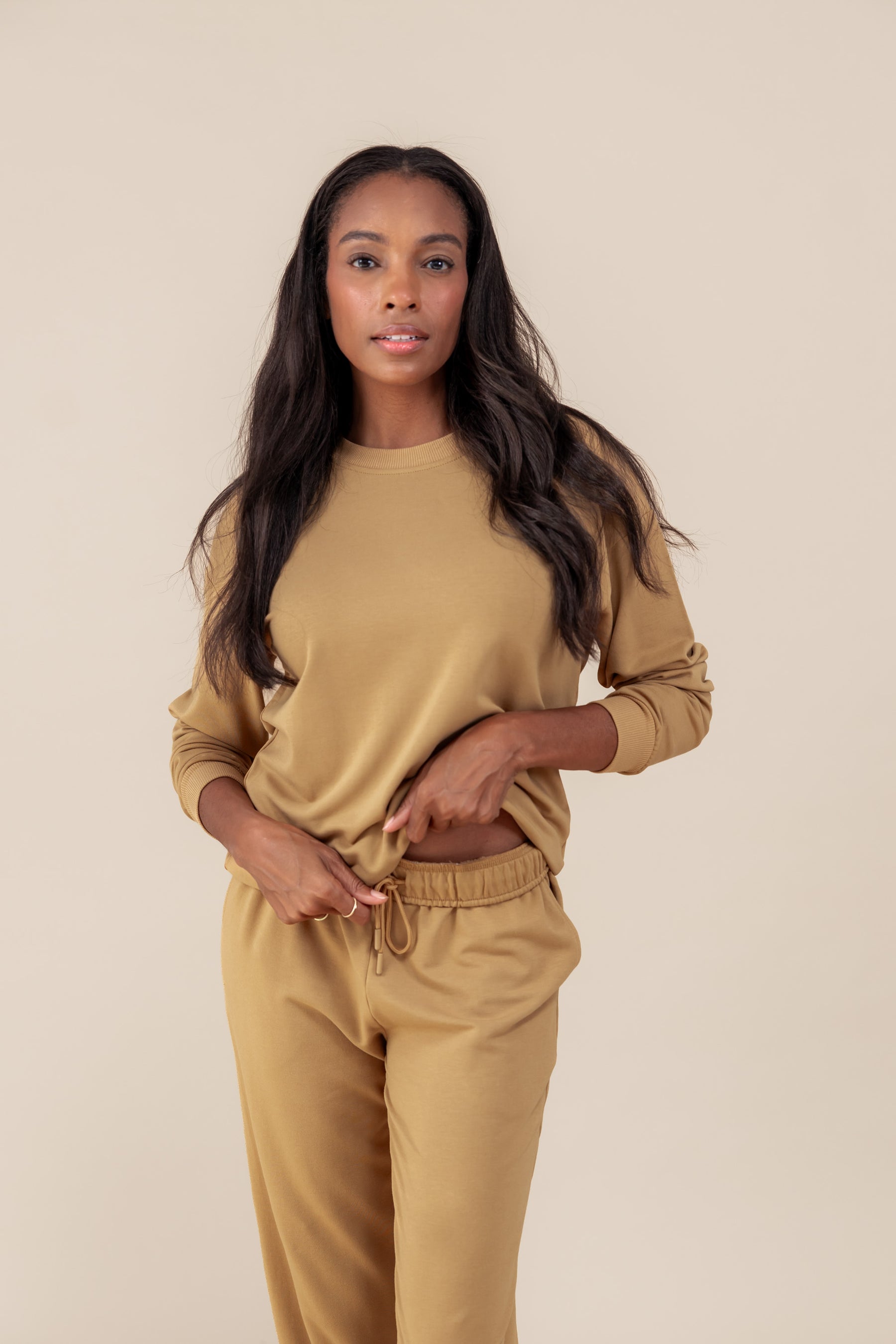 Woman wearing Women's Sweatshirt in Ochre color over similar color jogger pants on a beige background