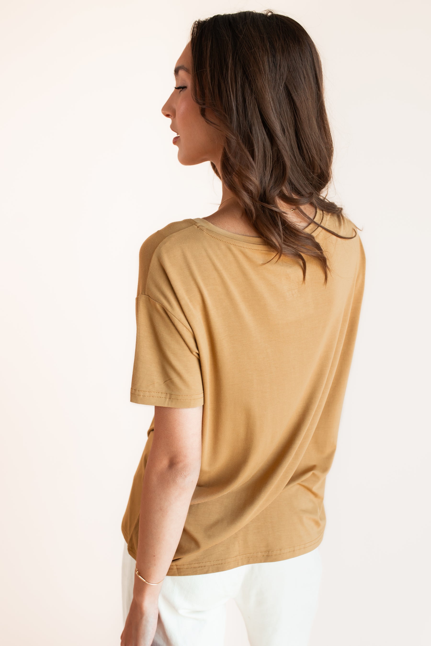 Model showcasing backside of Women's Oversized V-Neck Tee in Ochre over white pants on a beige background