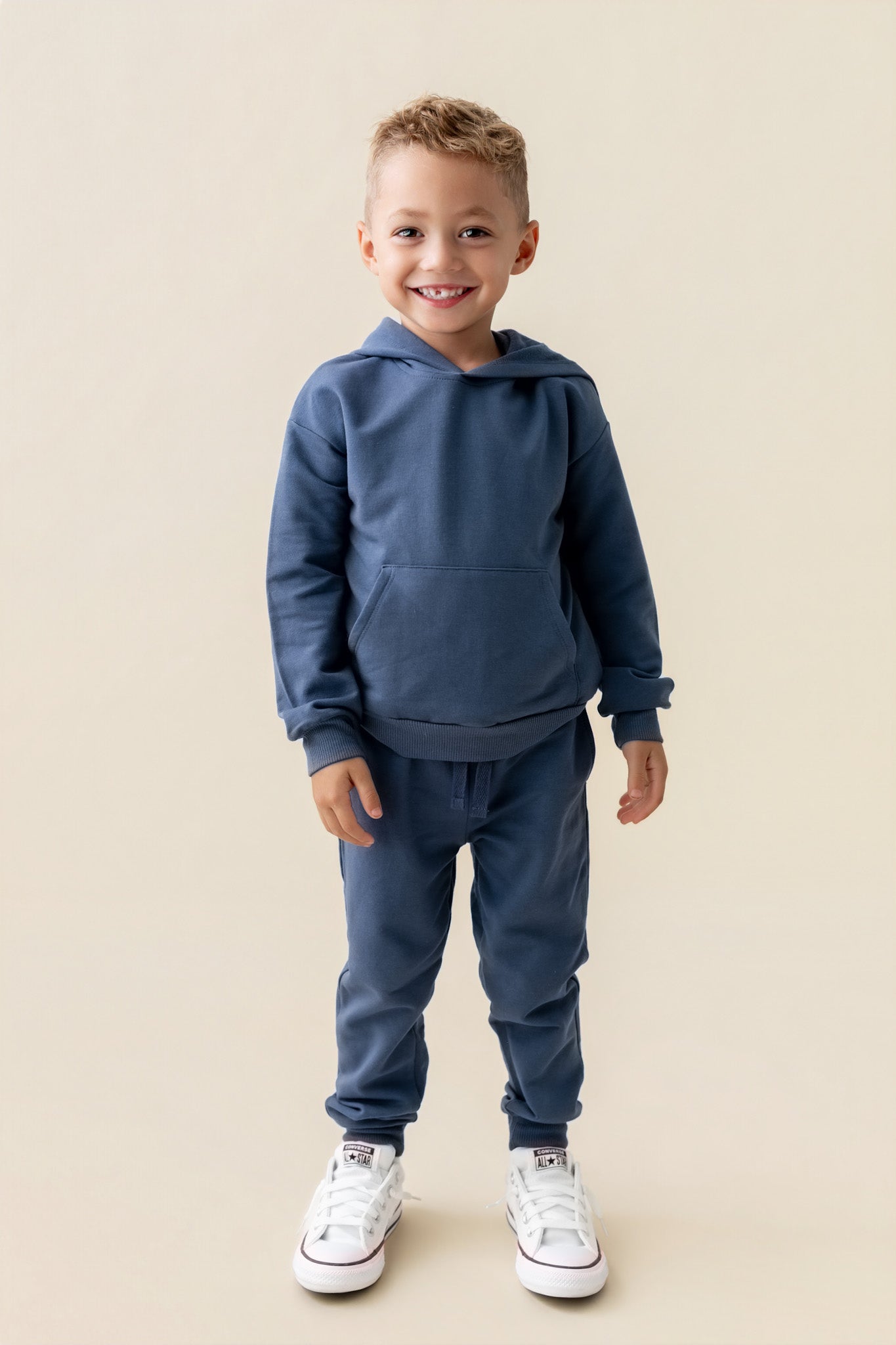 Boy wearing Hoodie in Oxford color and similar color jogger pants on a beige background