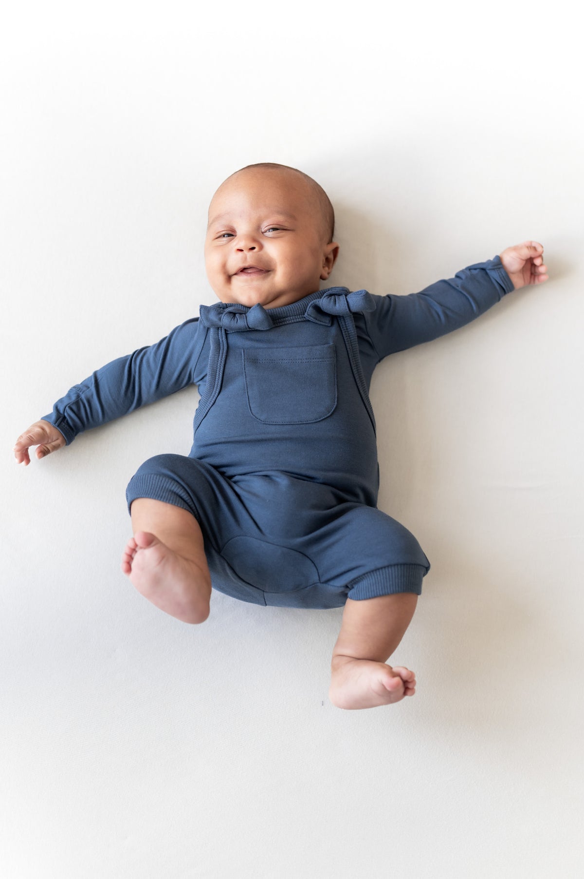 Baby wearing Overall in oxford color over similar color shirt lying on a beige background