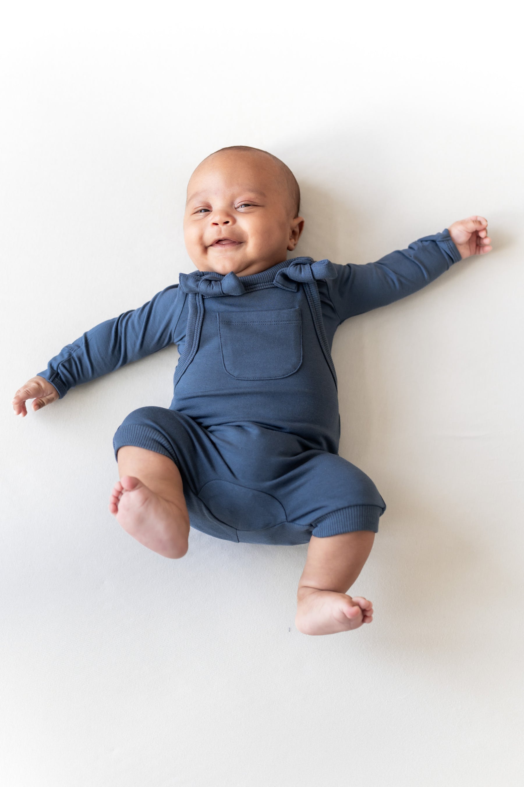 Baby wearing Overall in oxford color over similar color shirt lying on a beige background