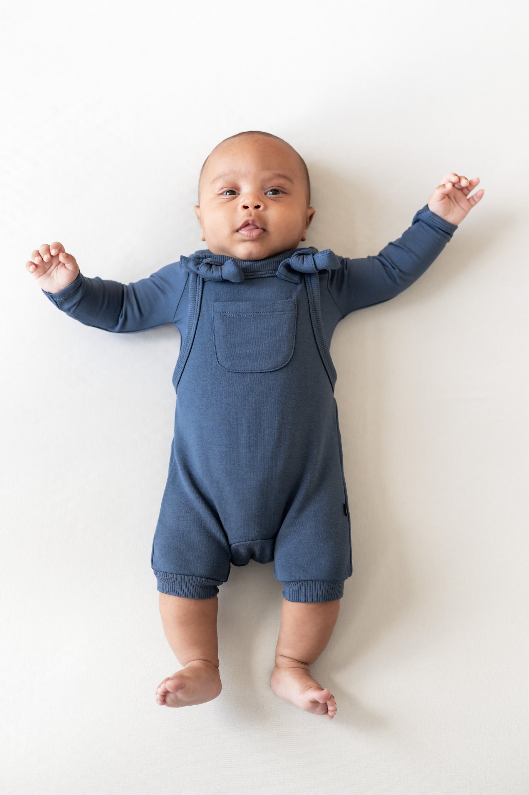 Baby wearing Overall in oxford color over similar color shirt on a beige background
