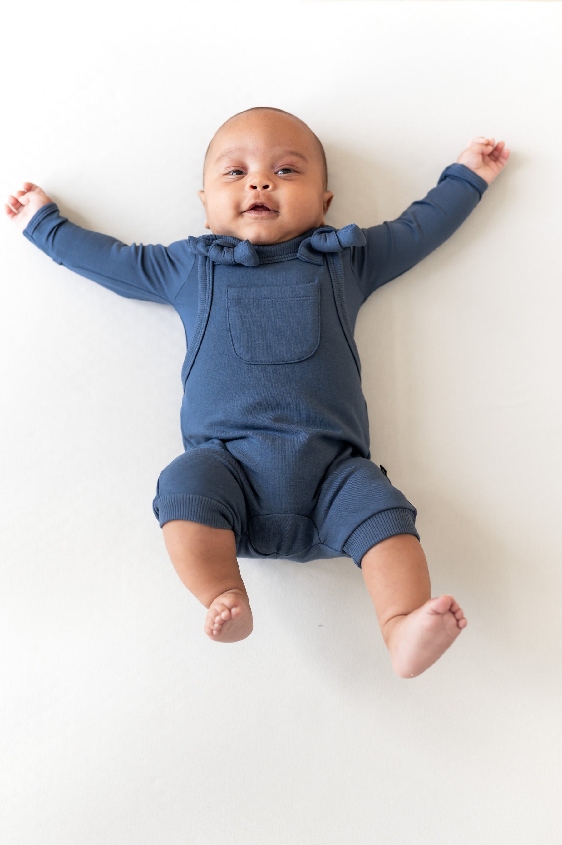 Baby wearing Overall in oxford color over similar color shirt lying on a beige background