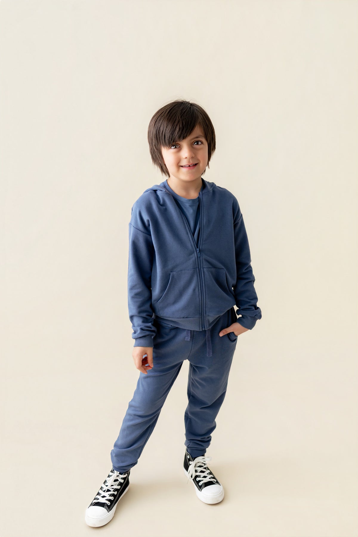 Boy wearing Hoodie in Oxford color and similar color jogger pants on a beige background
