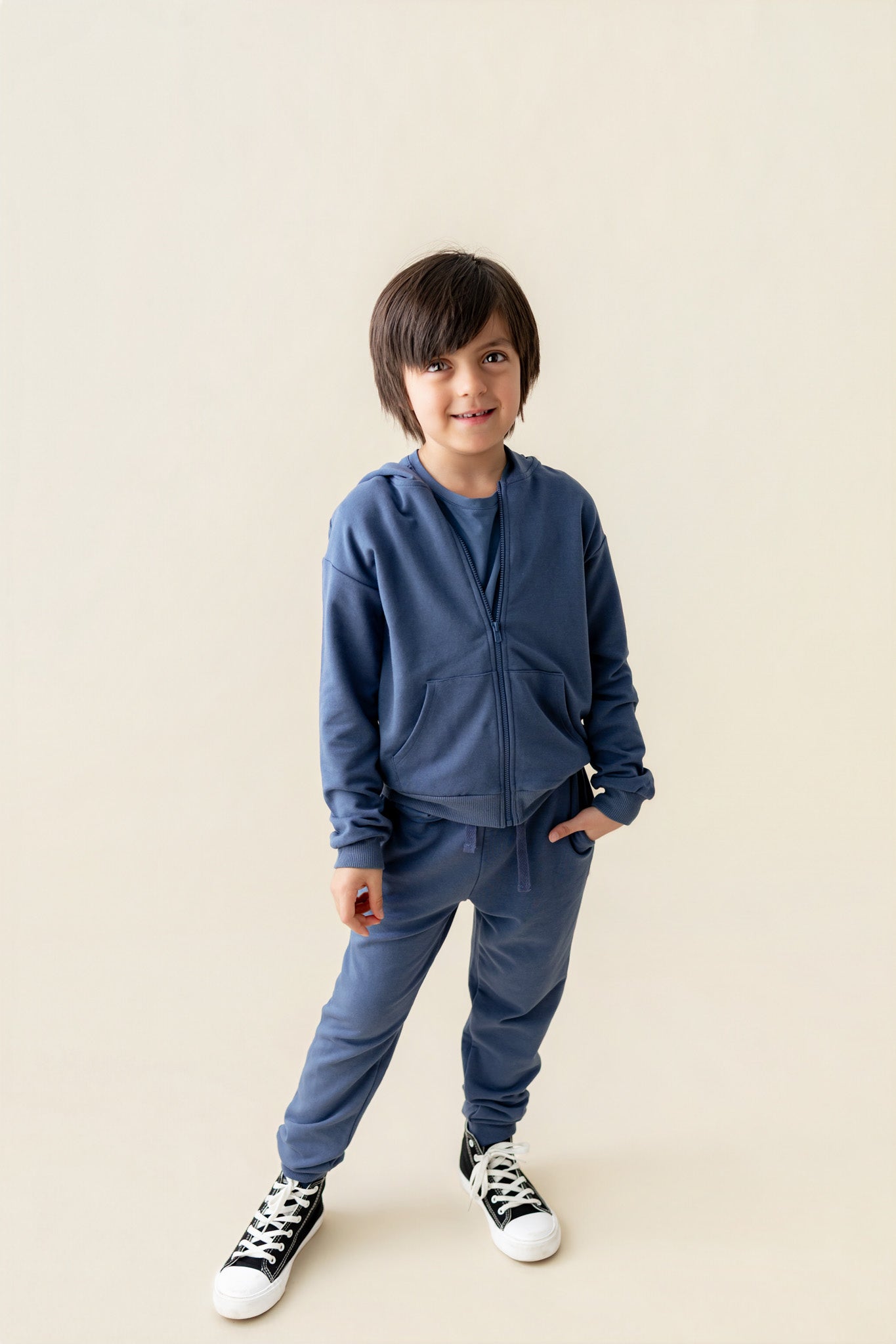 Boy wearing Hoodie in Oxford color and similar color jogger pants on a beige background