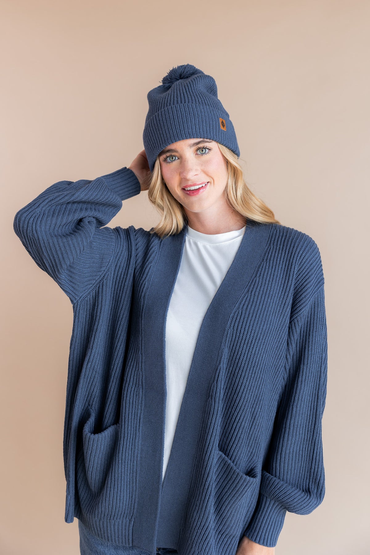 Modal wearing Chunky Knit Adult Pom in Oxford over Chunky knit cardigan in oxford and white T-shirt on a beige background