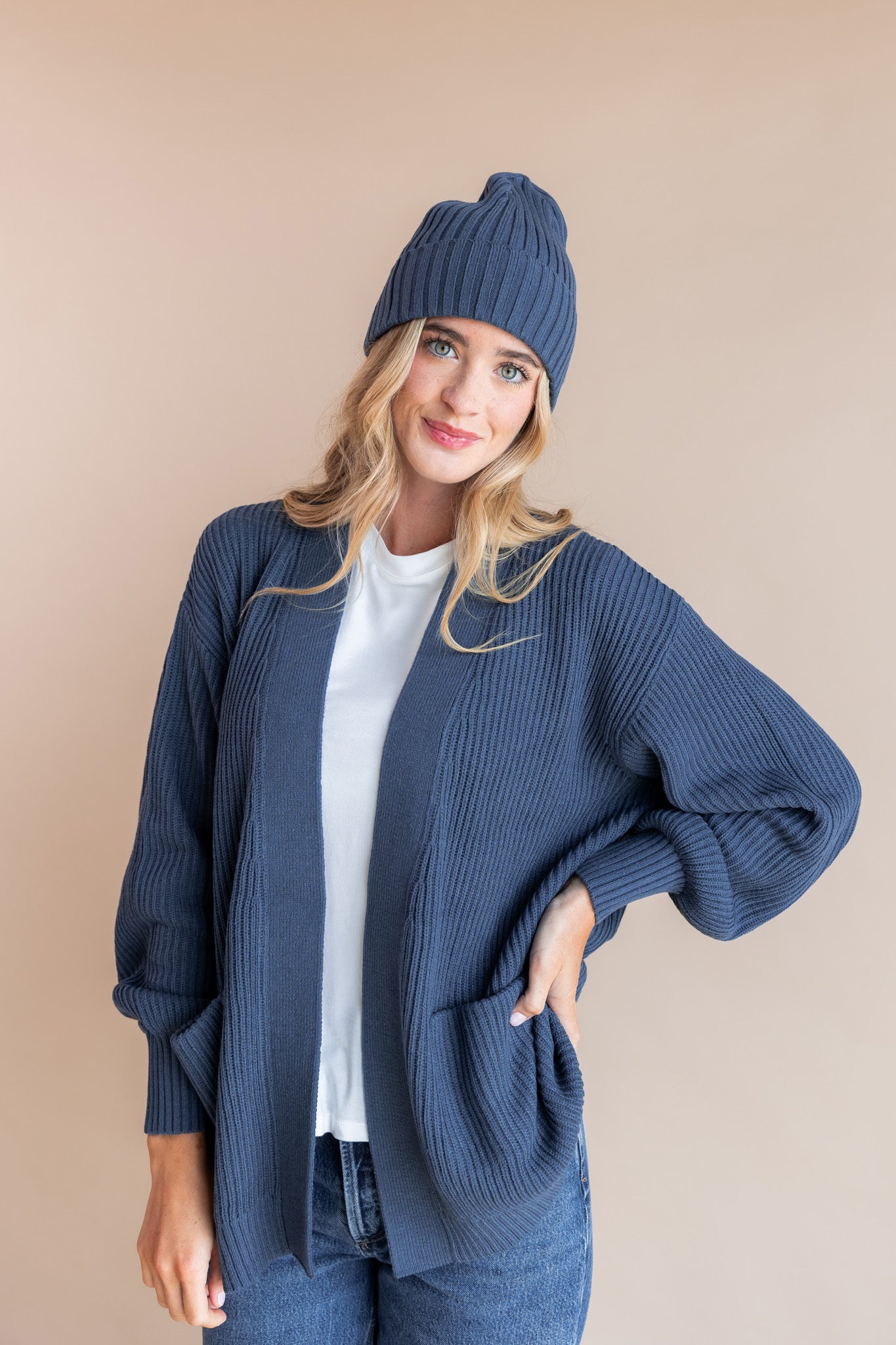 Modal posing in Chunky Knit Adult Ribbed Beanie in Oxford over white T-shirt and Chunky knit cardigan in oxford on a beige background