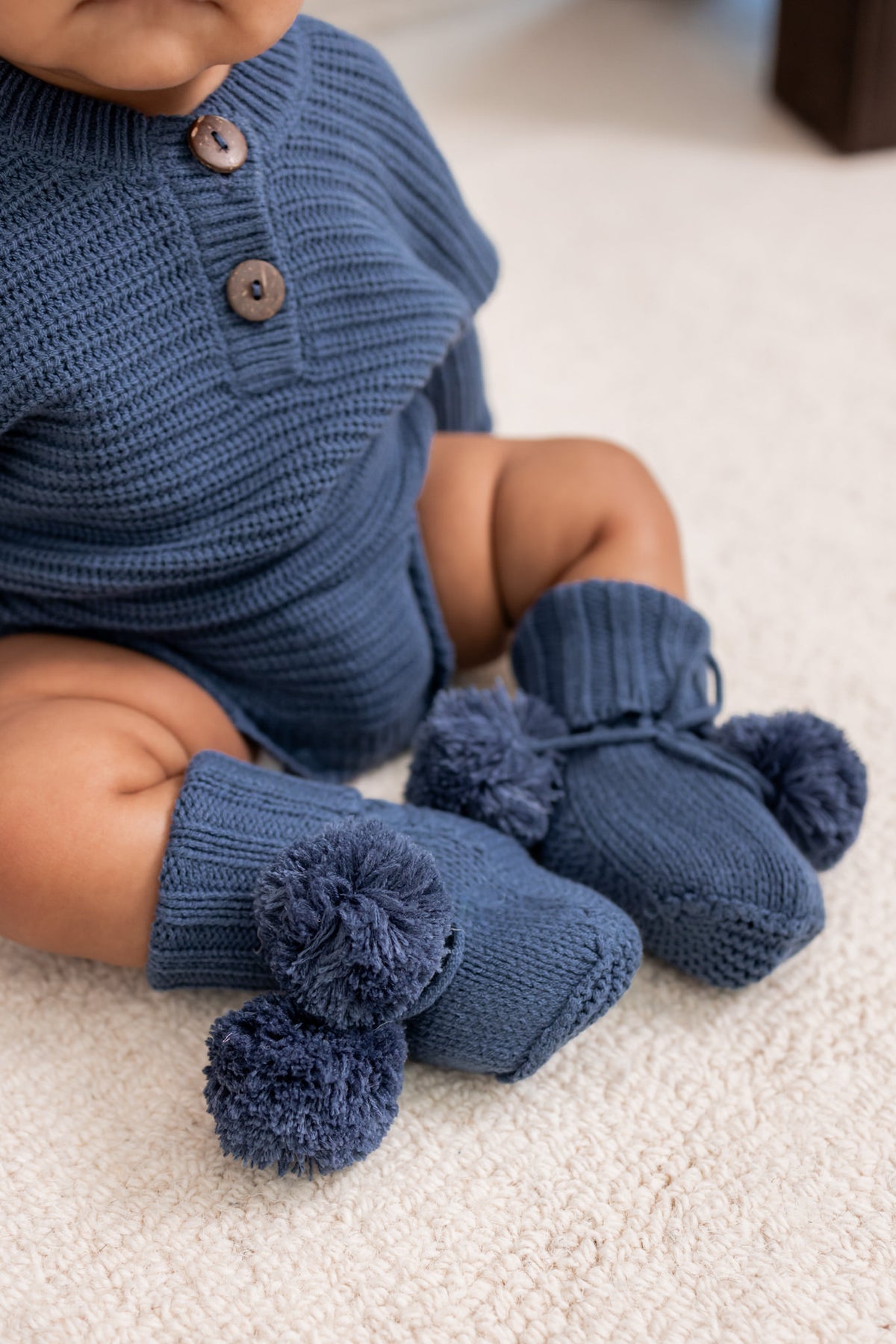 Baby wearing Knit Booties and Chunky knit romper in Oxford on a white carpet