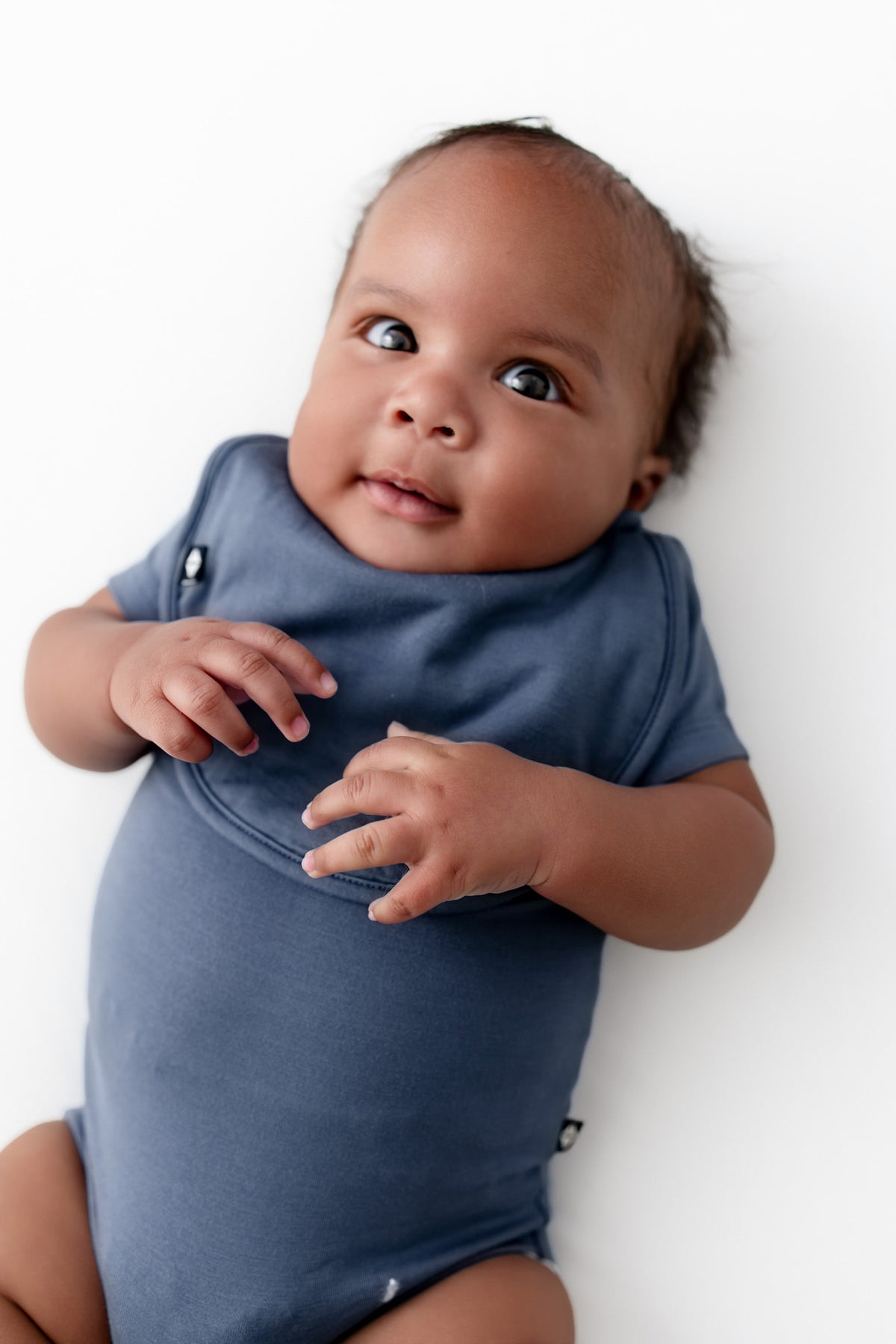 Baby wearing Cushy Bib in Oxford over similar color bodysuit on a white background