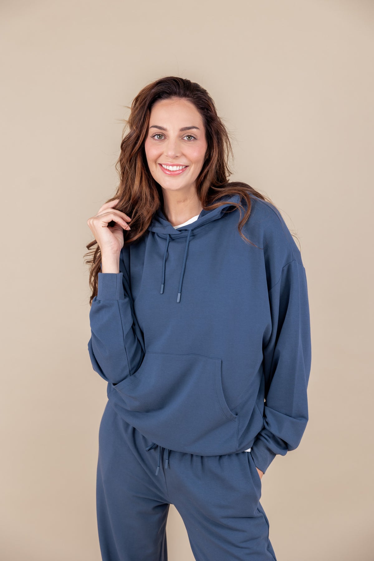 Woman wearing Women's Hoodie in Oxford color over similar color sweatpants on a beige background