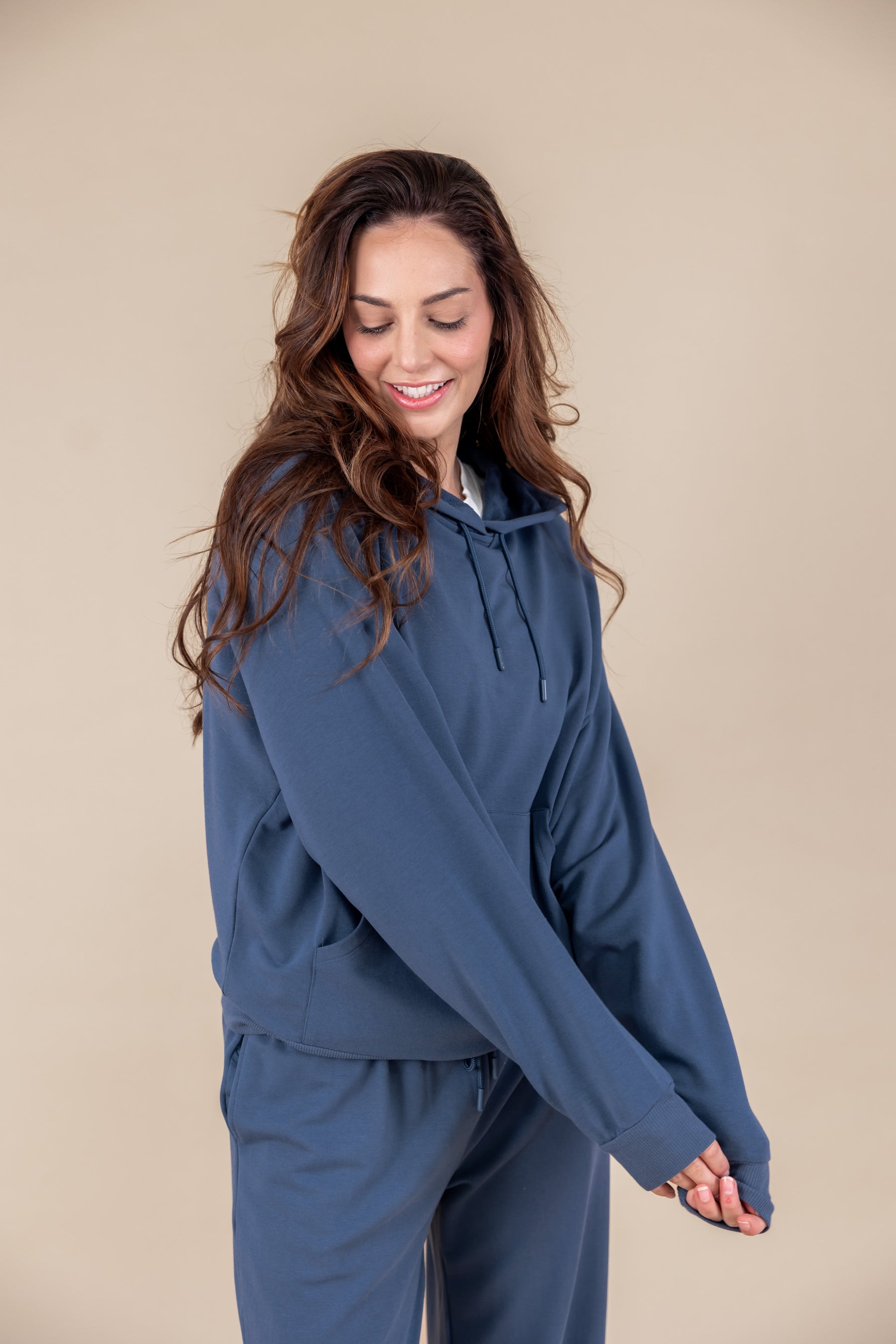 Woman posing in Women's Hoodie in Oxford color over similar color sweatpants on a beige background