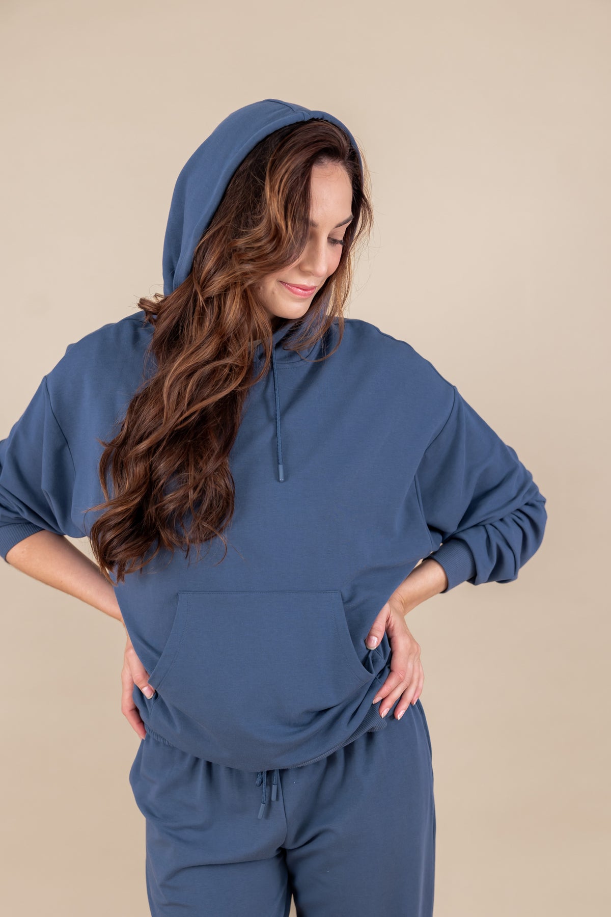 Woman posing in Women's Hoodie in Oxford color over similar color sweatpants on a beige background
