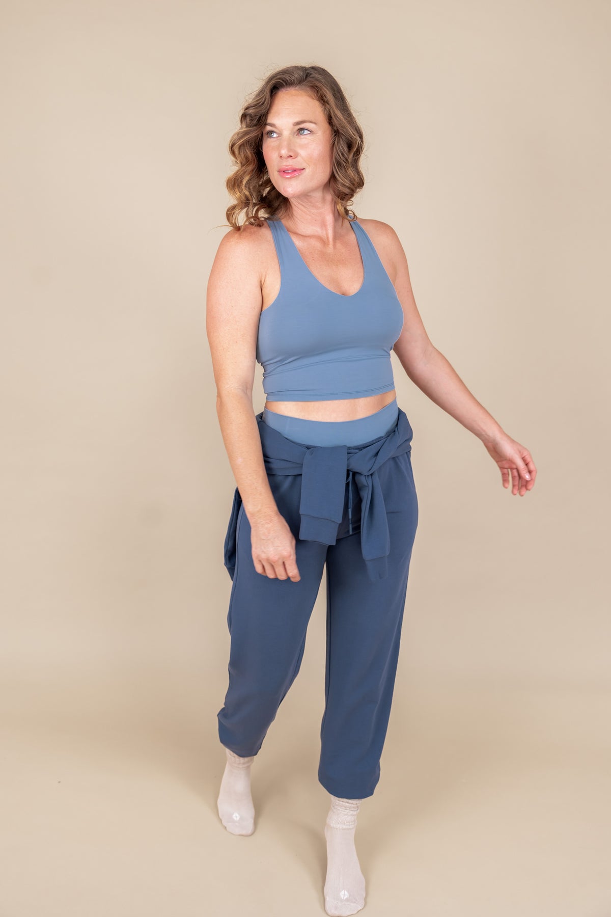 Modal wearing Women's Jogger Pants in Oxford color under flex Bra tank in breeze and sweatshirt on waist on a beige background