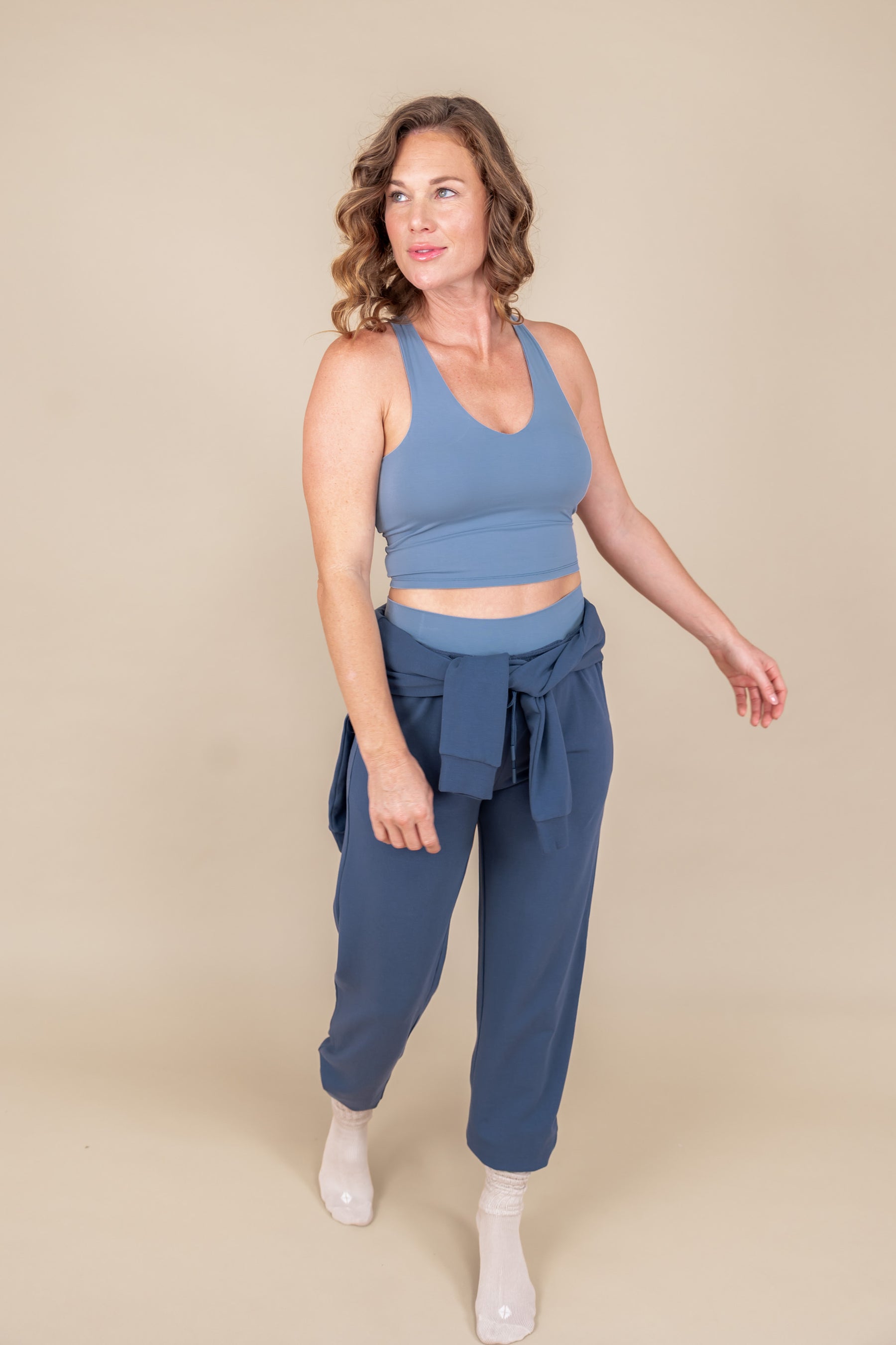 Modal wearing Women's Jogger Pants in Oxford color under flex Bra tank in breeze and sweatshirt on waist on a beige background